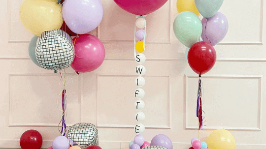 Colorful balloon arrangement featuring a large gold numerical '2' balloon, a red airplane balloon, and various other balloons in red, yellow, and metallic colors from The Sky Balloons