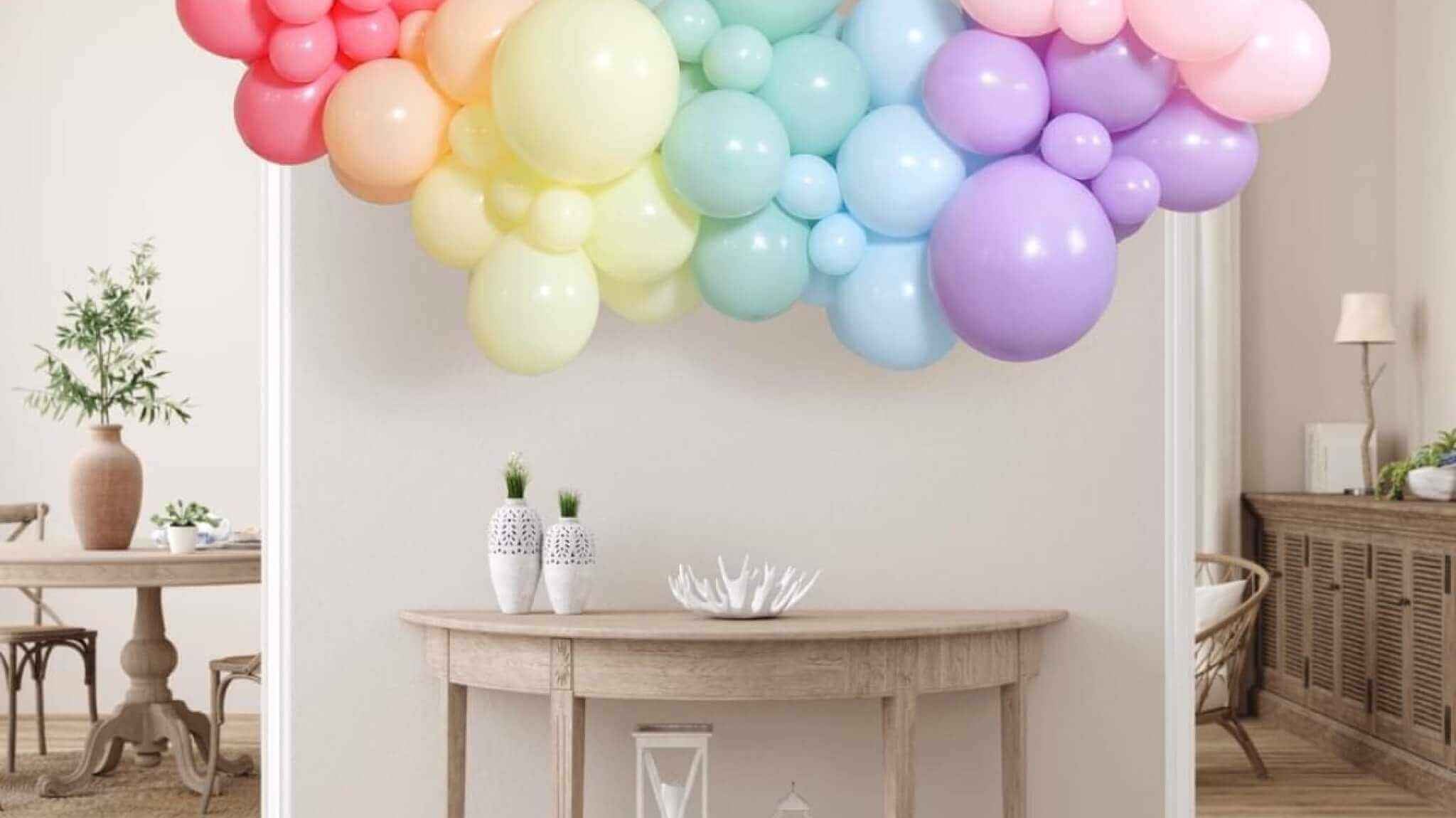 Colorful organic balloon garland decor by The Sky Balloons, featuring a mix of pastel-colored balloons arranged in a stylish, natural flow above a wooden console table in a modern living room setting.