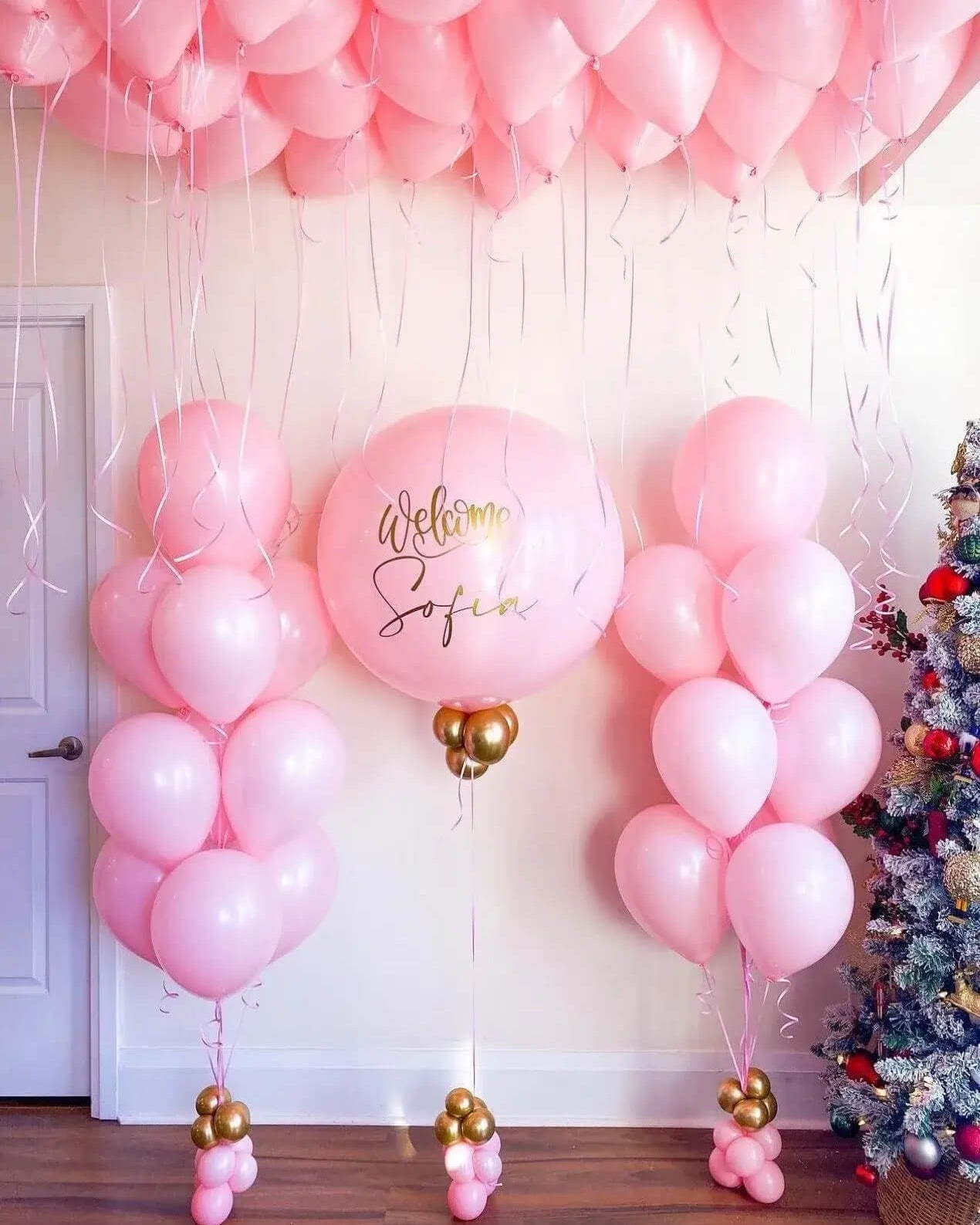 Pink balloon arch with 'Welcome Sofia' text, Christmas tree on right