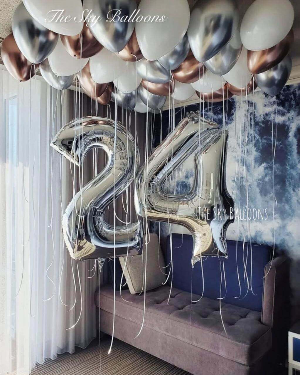 24th birthday celebration balloon setup with metallic silver and chrome balloons covering bedroom ceiling with large number 24 balloons