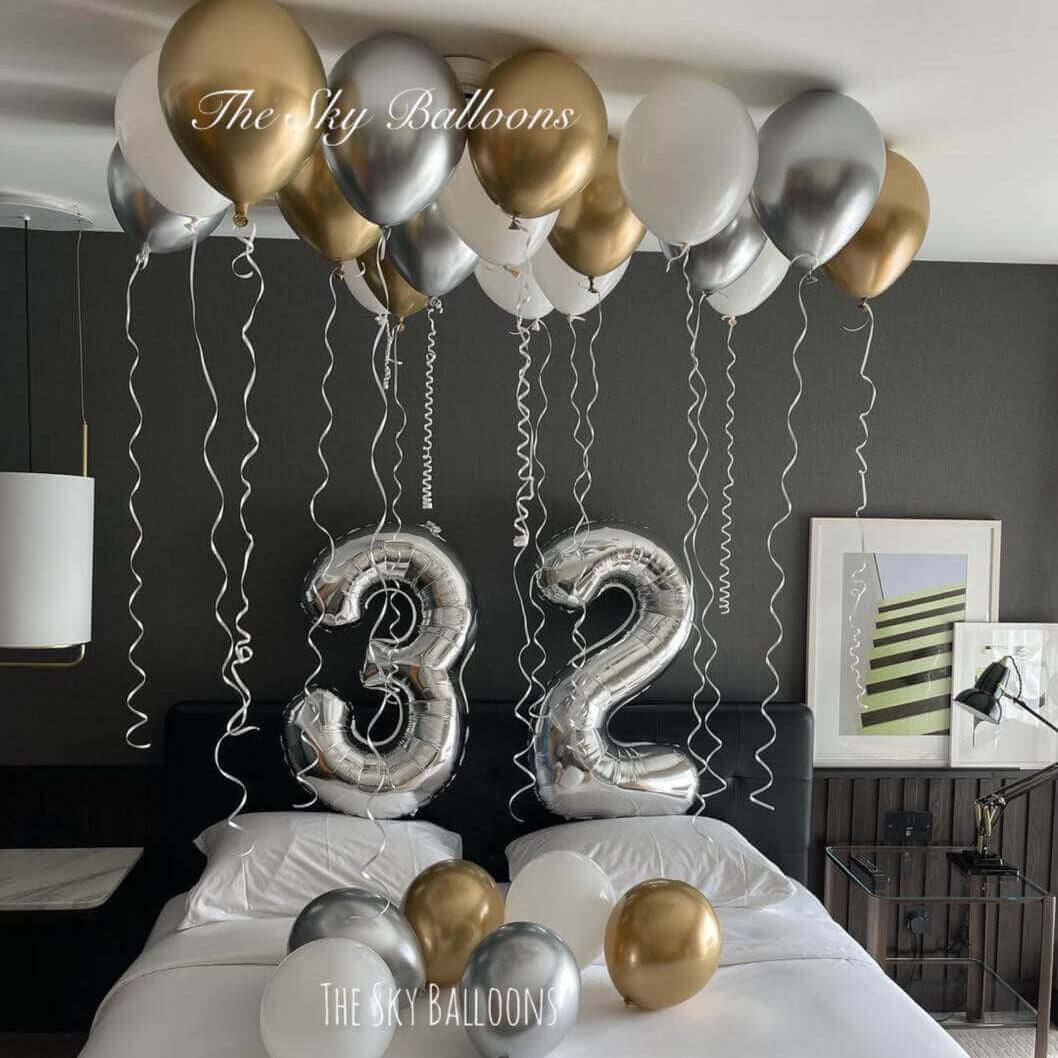 32nd birthday luxury balloon setup with gold, silver and white balloons covering ceiling and large number 32 balloons in bedroom