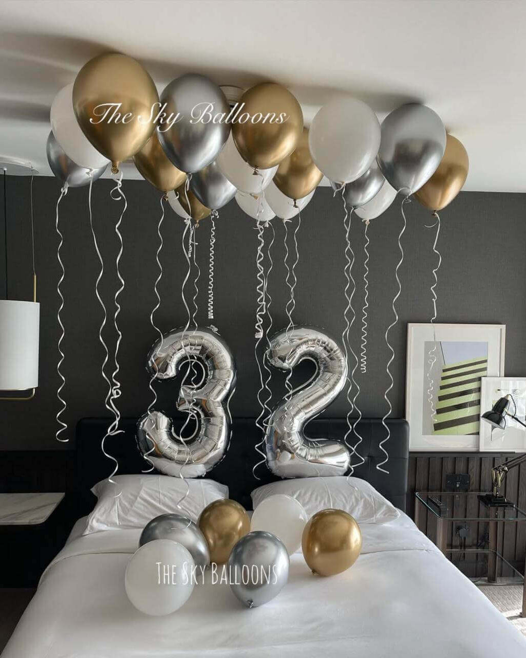 32nd birthday luxury balloon setup with gold, silver and white balloons covering ceiling and large number 32 balloons in bedroom