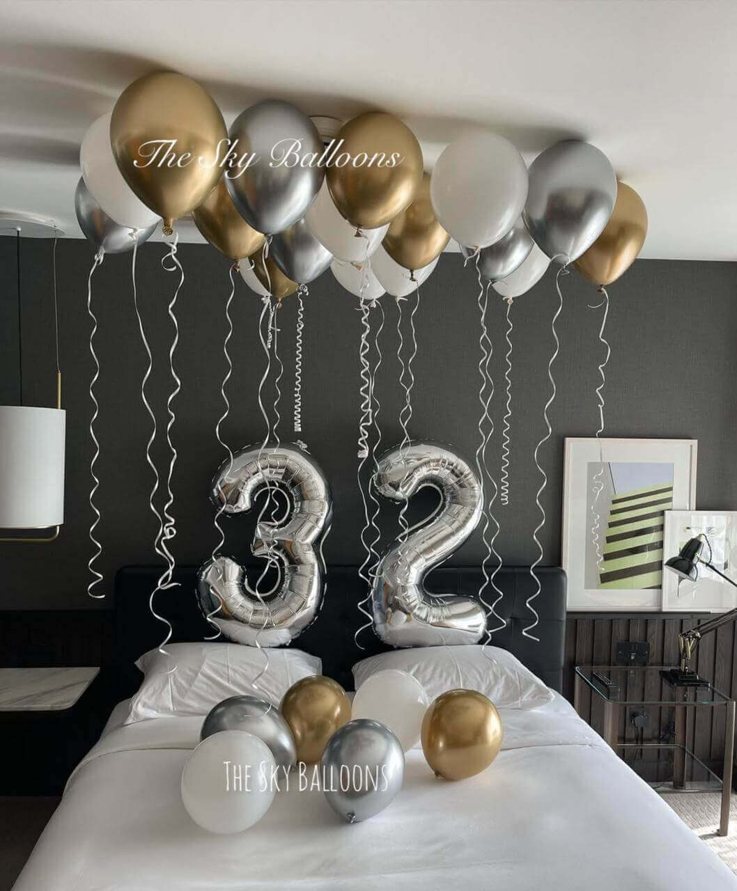 32nd birthday luxury balloon setup with gold, silver and white balloons covering ceiling and large number 32 balloons in bedroom