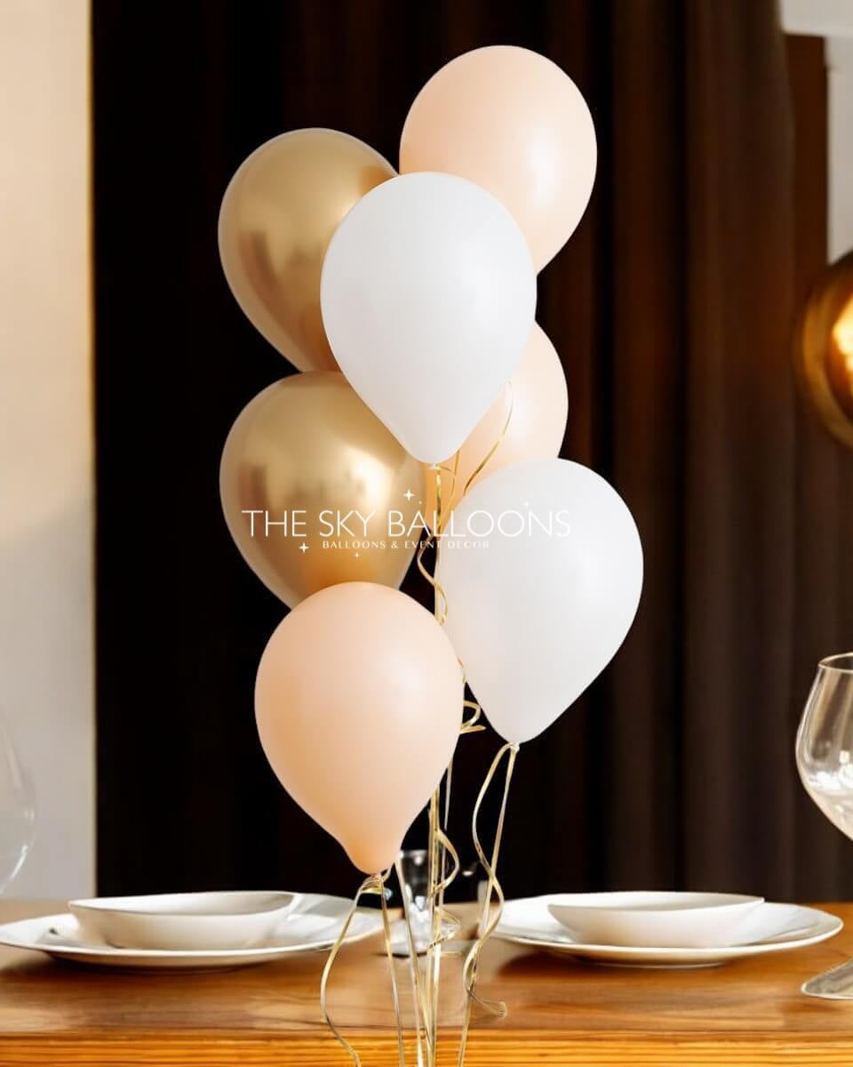 A bouquet of helium-filled balloons in various colors, including gold, white, and pink, tied together and placed on a table.