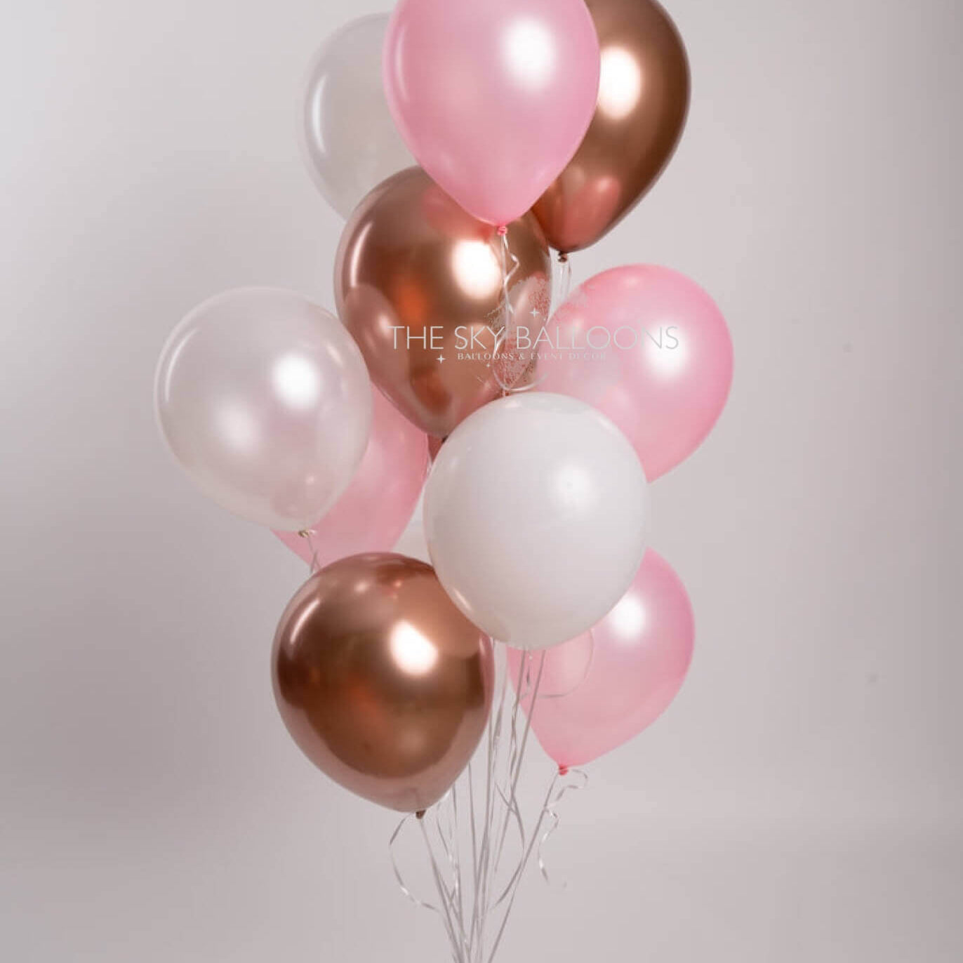A bunch of pink and rose gold latex balloons tied together with a string, against a white background.