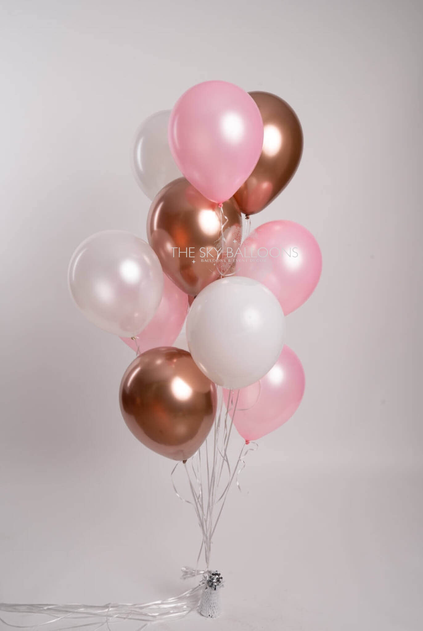 A bunch of pink and rose gold latex balloons tied together with a string, against a white background.