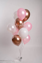A bunch of pink and rose gold latex balloons tied together with a string, against a white background.