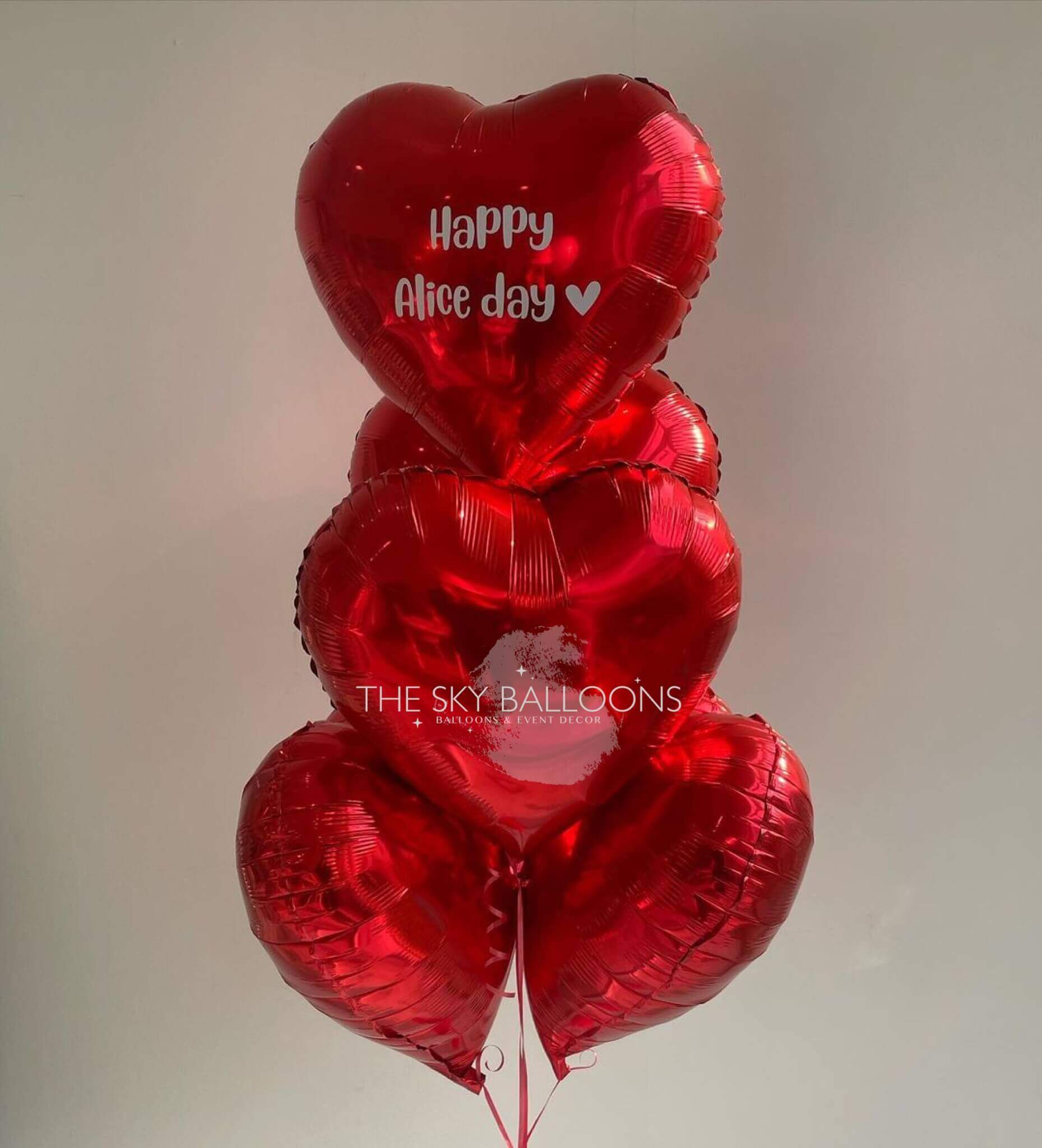 A bunch of red heart-shaped foil balloons with 'Happy Anniversary' written on one of them, tied together.