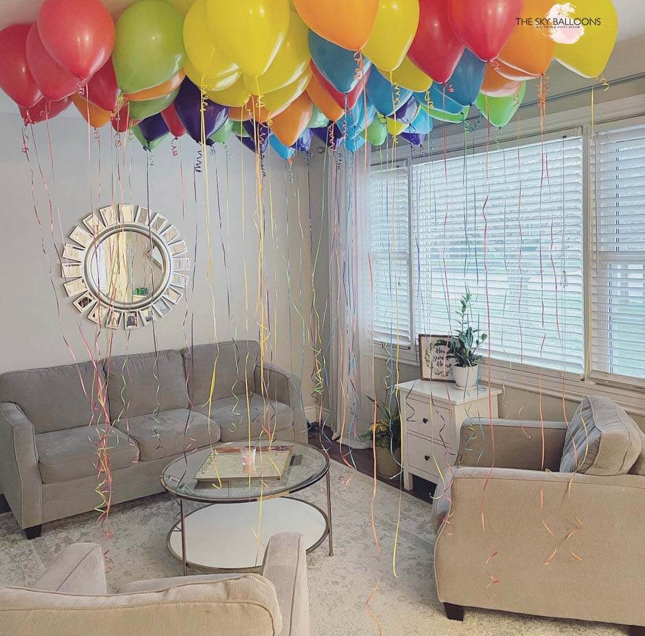 A living room decorated with multicolored helium ceiling balloons creating a festive atmosphere.