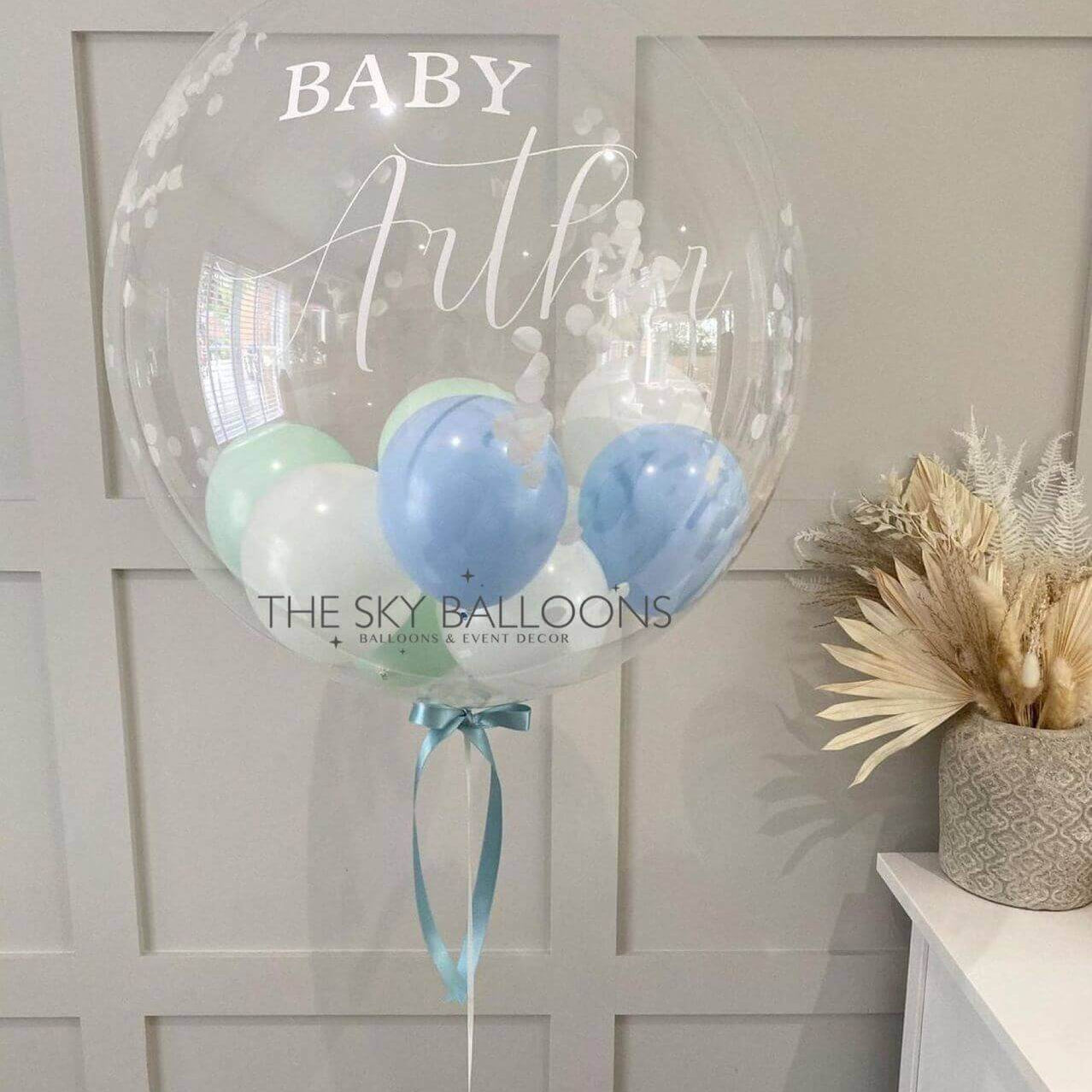 A custom-printed balloon with the name 'Baby Authur' in a clear font, attached to a blue ribbon, with two smaller blue balloons inside.