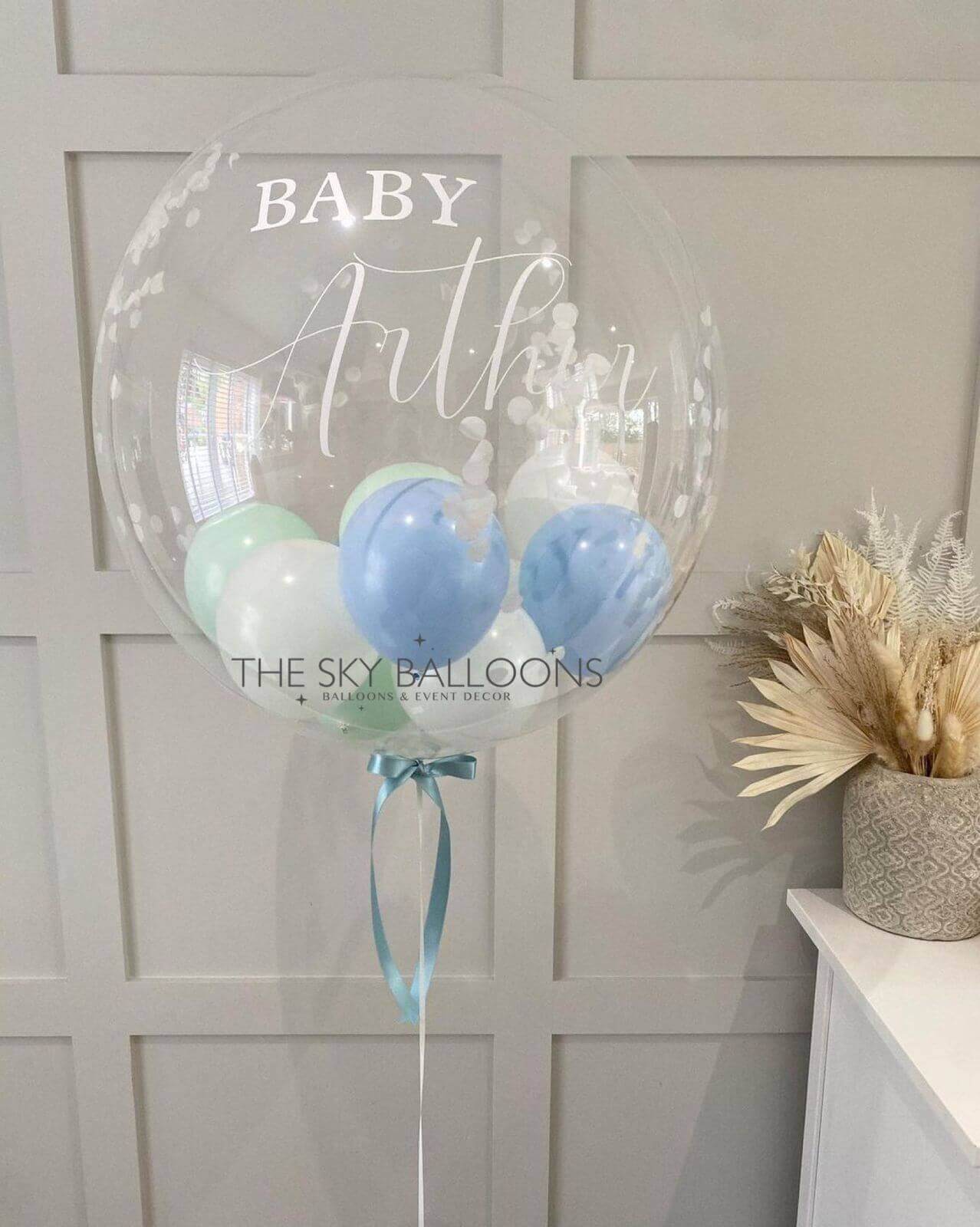 A custom-printed balloon with the name 'Baby Authur' in a clear font, attached to a blue ribbon, with two smaller blue balloons inside.