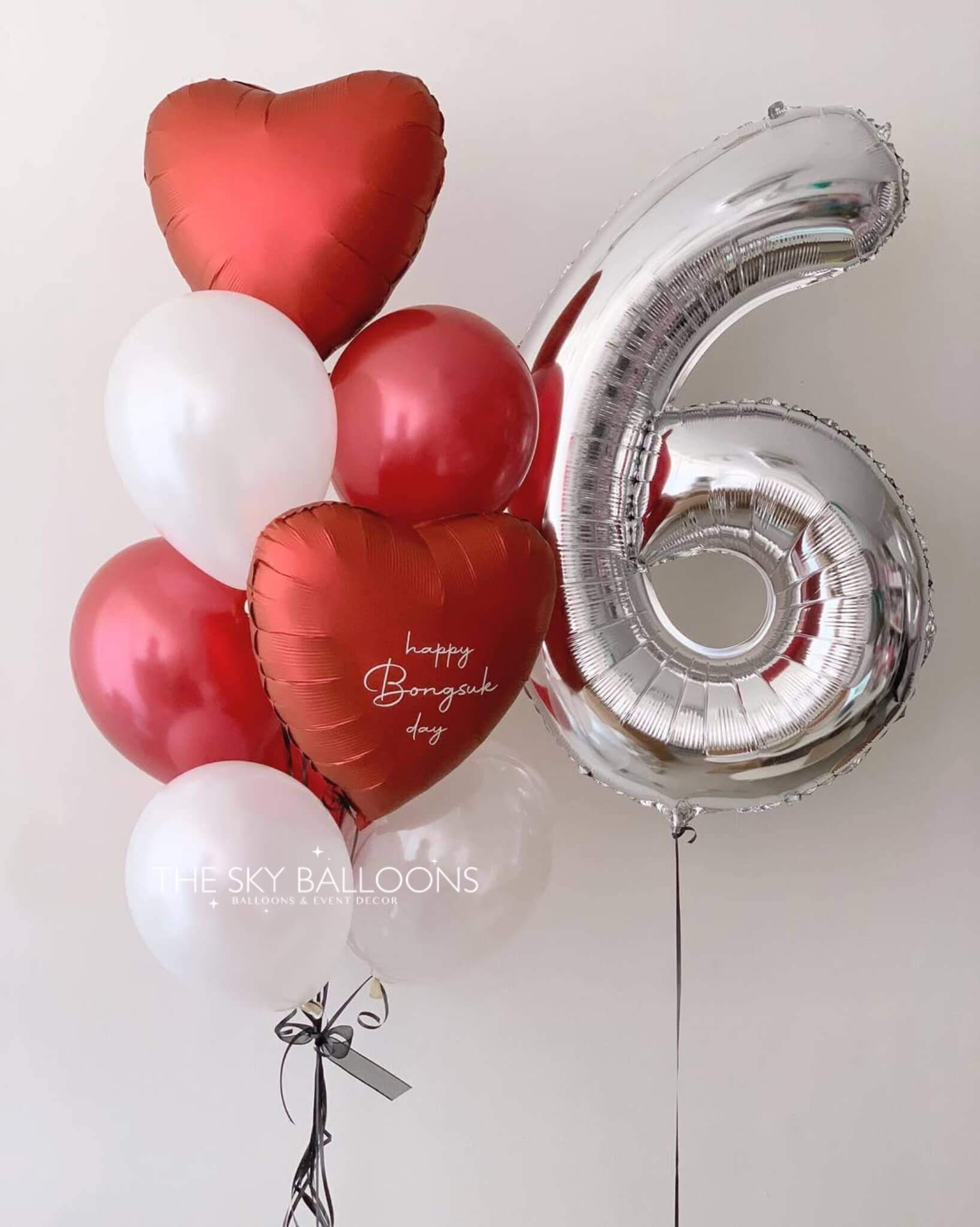 A colorful balloon bouquet featuring a large number six surrounded by red heart-shaped balloons.