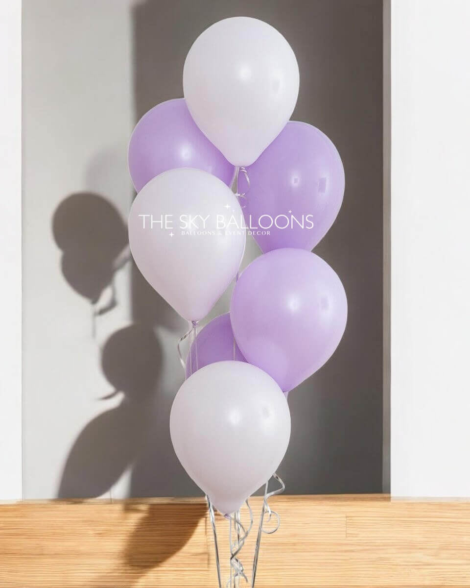 A bouquet of helium-filled purple and white balloons tied together, with the shadow of a person holding a camera reflected on the wall in the background.
