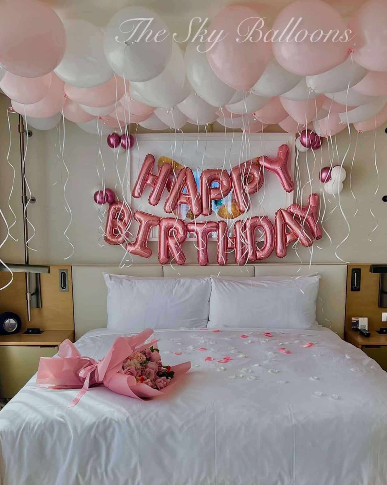 Bedroom decorated with pink and white balloons, 'Happy Birthday' sign, and flowers.