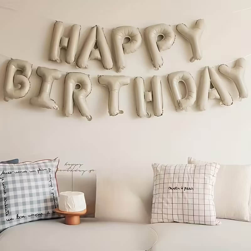 Balloon letters spelling 'Happy Birthday' on a wall above a sofa with decorative pillows.