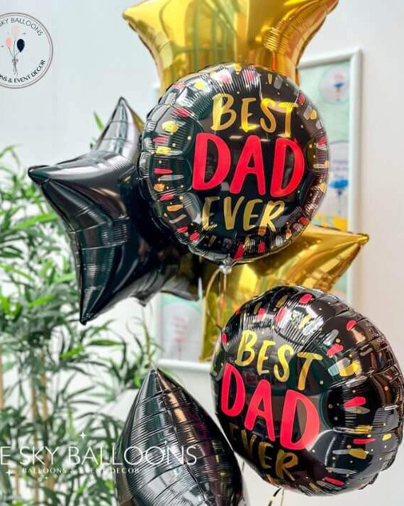 A set of helium-filled balloons, with two larger round balloons reading 'BEST DAD EVER' in red and black, and four star-shaped balloons in gold and black. All balloons are inflated and arranged together.