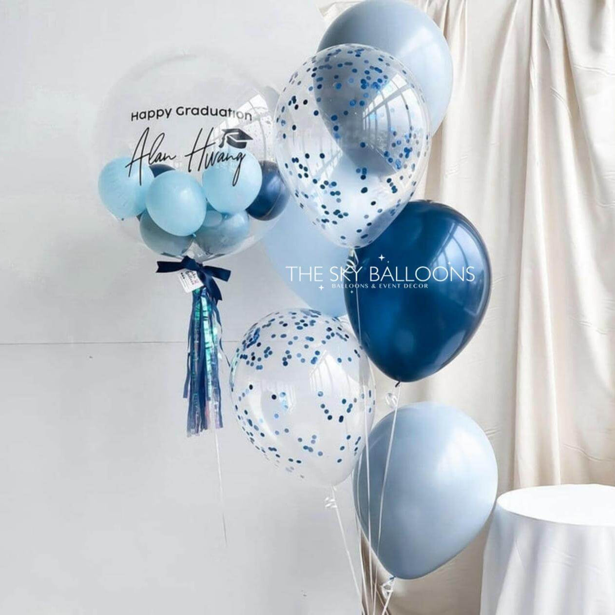 Blue and white balloons with confetti on a white background, featuring 'The Sky Balloons' branding.