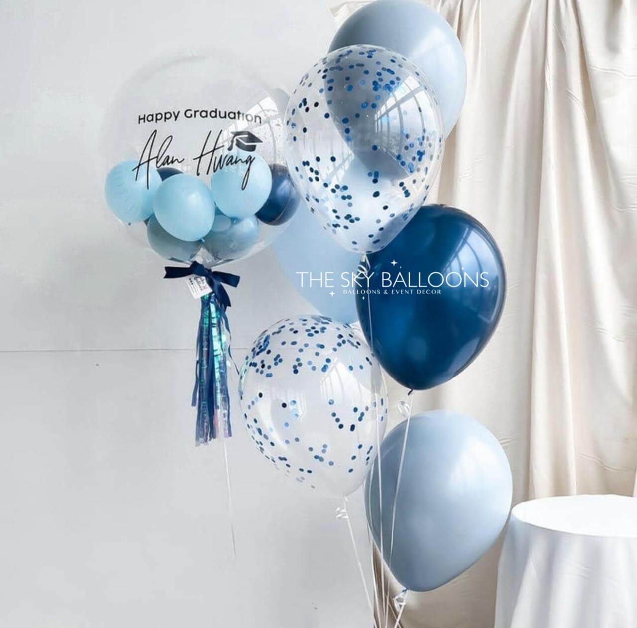 Blue and white balloons with confetti on a white background, featuring 'The Sky Balloons' branding.