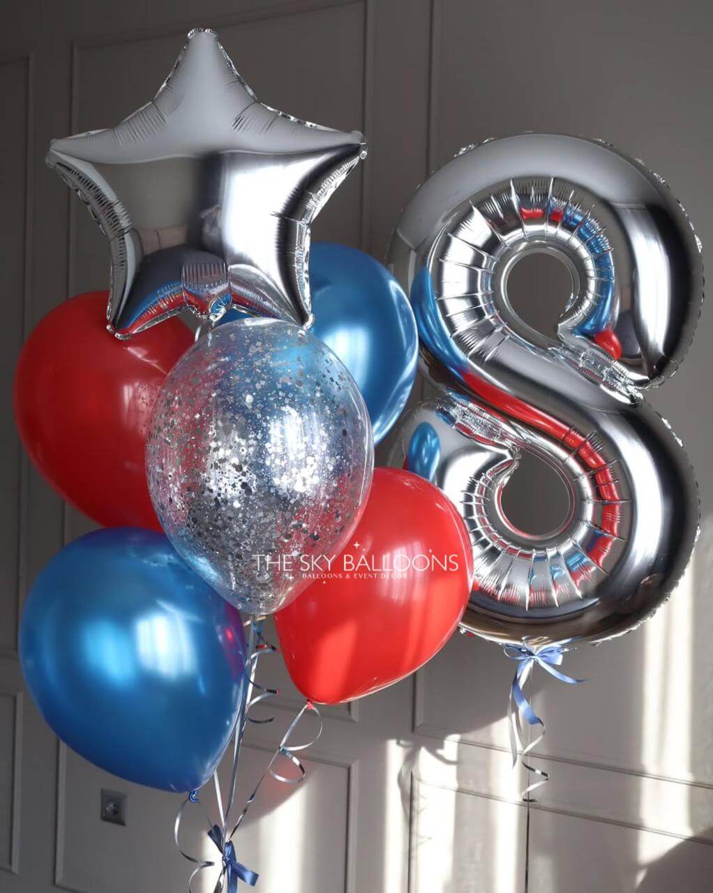 Bouquet of balloons including a silver star, number 8 balloon, red heart, and blue balloons against a neutral background.
