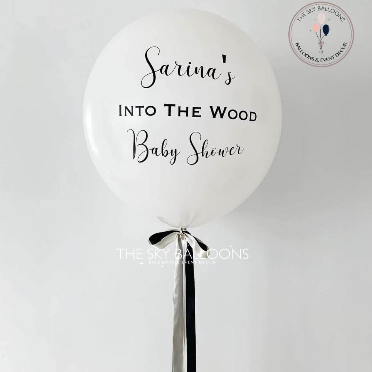 White balloon with black text 'Sarina's Into The Wood Baby Shower' on a white background
