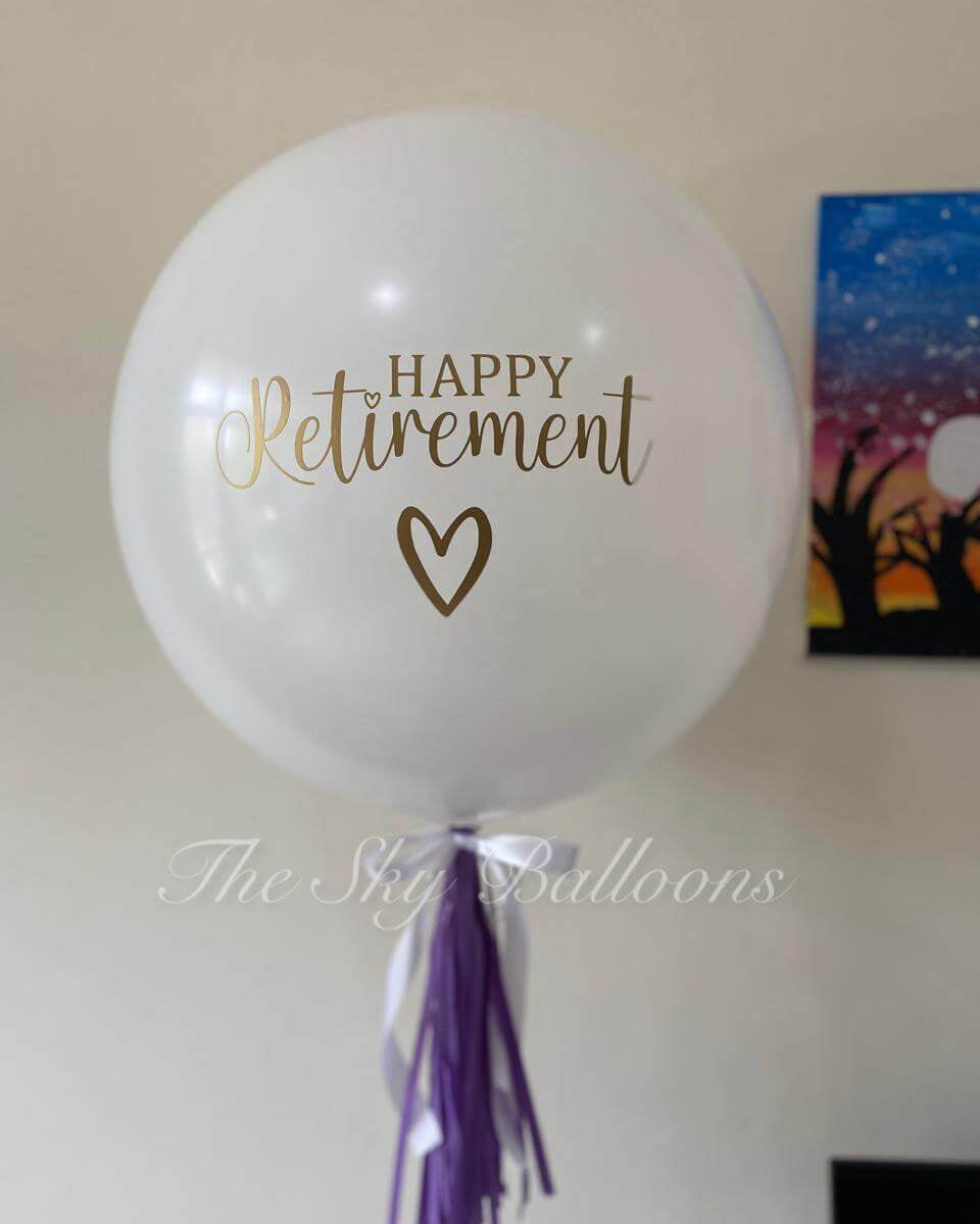 White balloon with 'Happy Retirement' text and heart symbol, featuring a purple tassel, on a plain background.