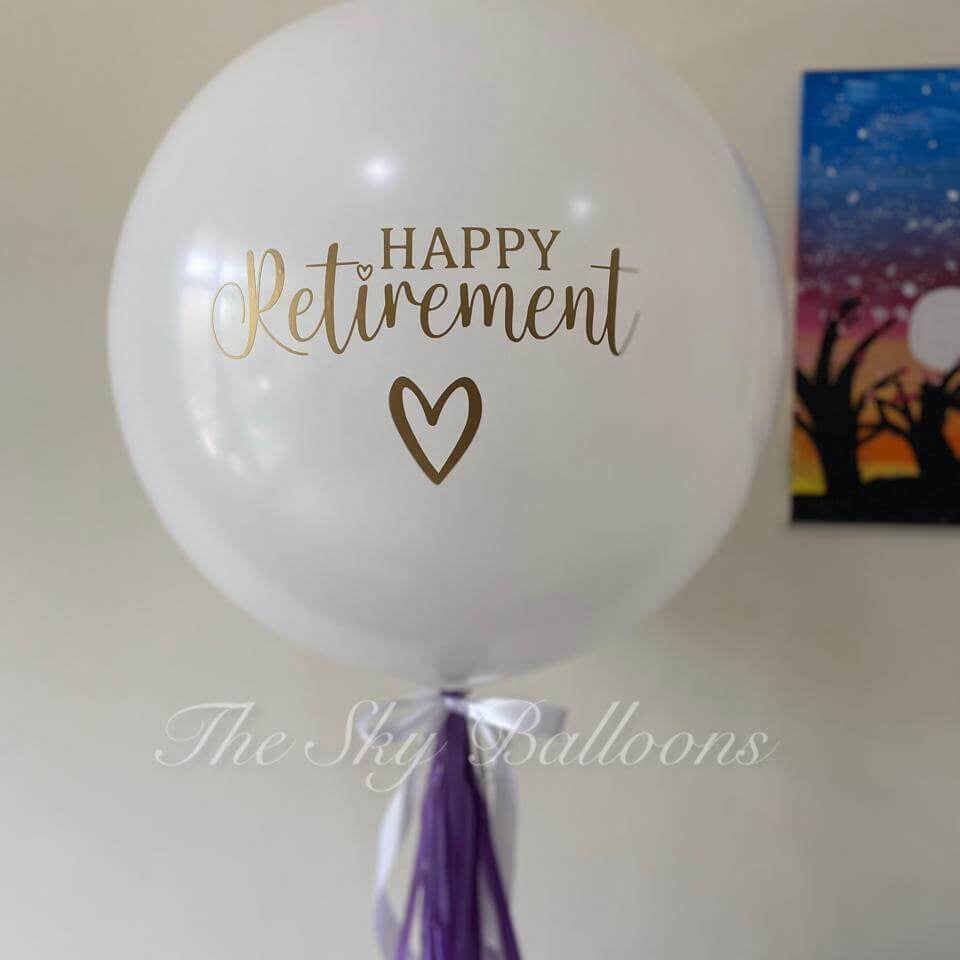 White balloon with 'Happy Retirement' text and heart symbol, featuring a purple tassel, on a plain background.
