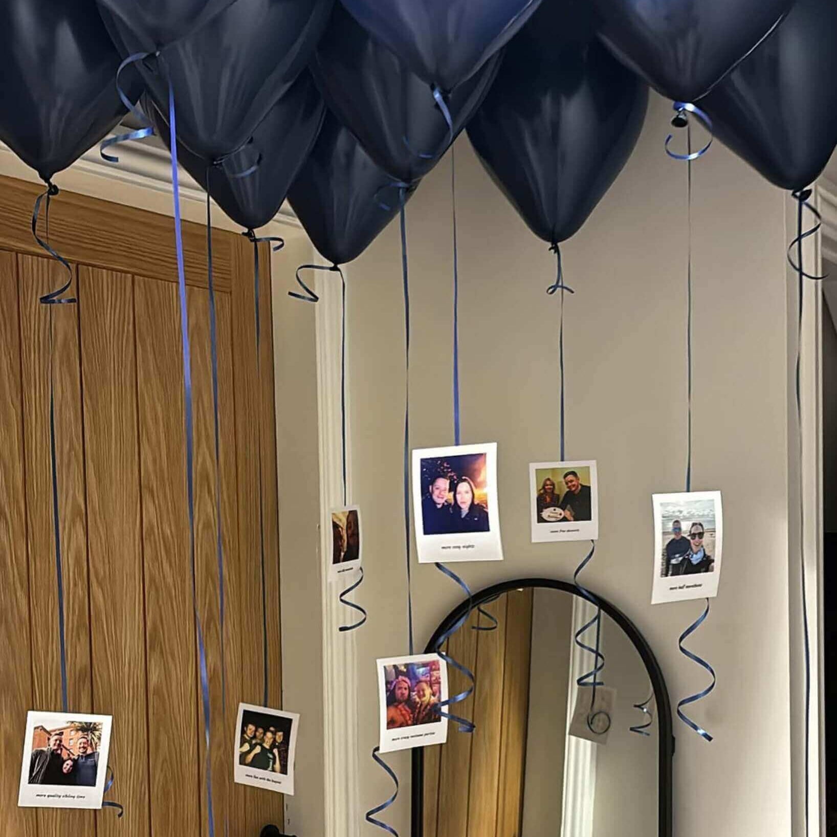 Nvay Blue balloons with blue strings attached to a mirror with photos hanging from them, labeled 'The Sky Balloons'.