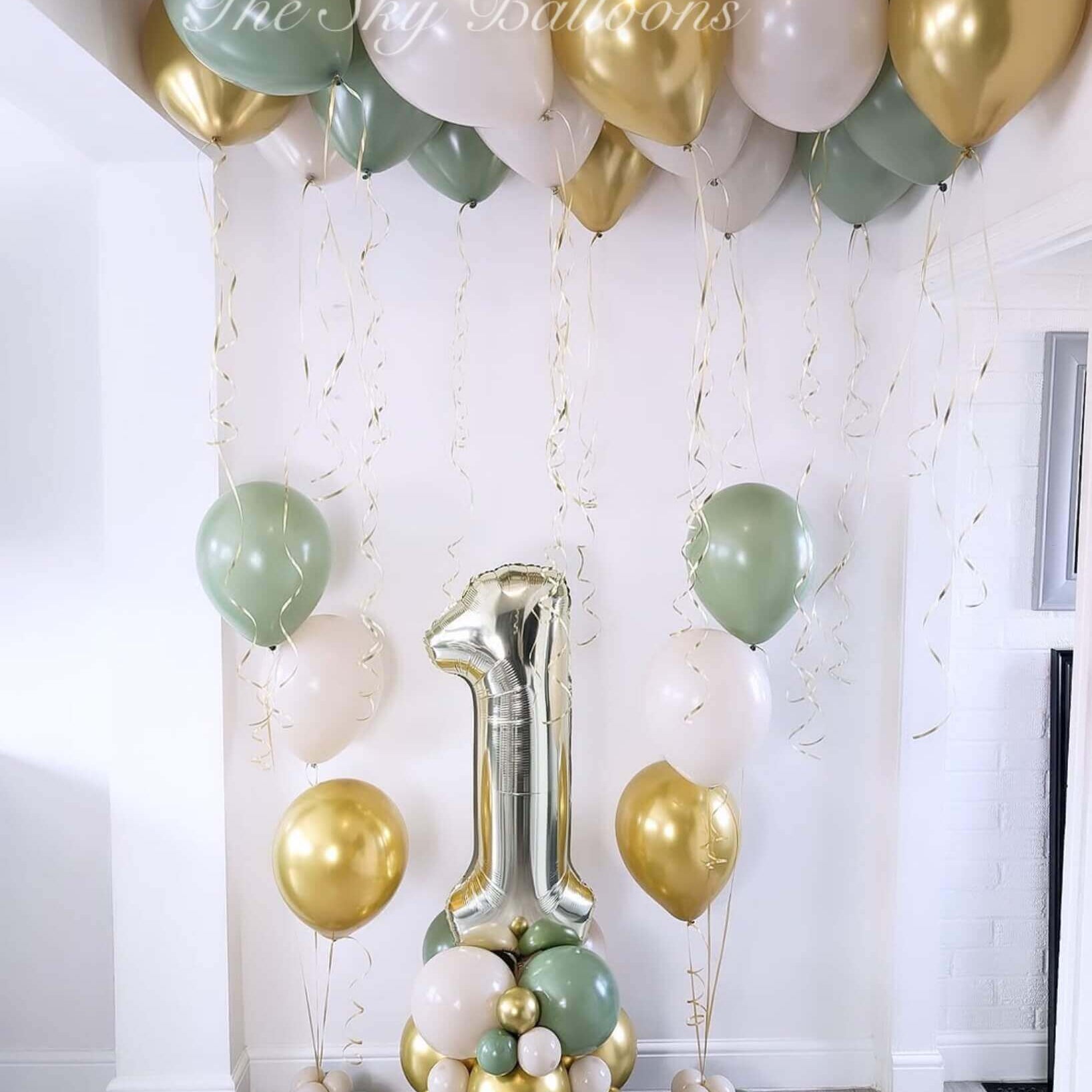 Decorative balloon arch with green, gold, and white balloons in a room.