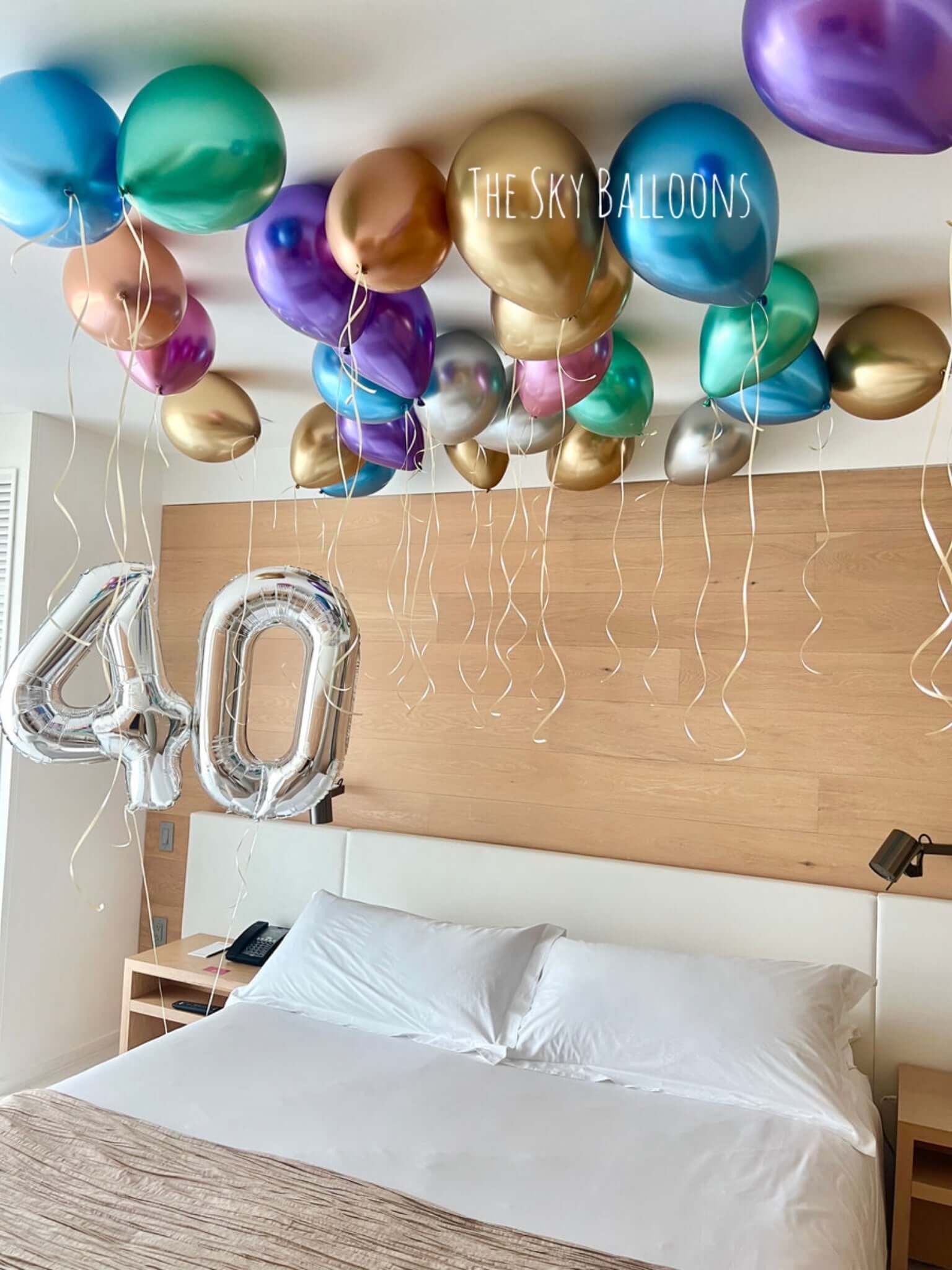 Decorative balloons and a '40' balloon over a bed in a room.