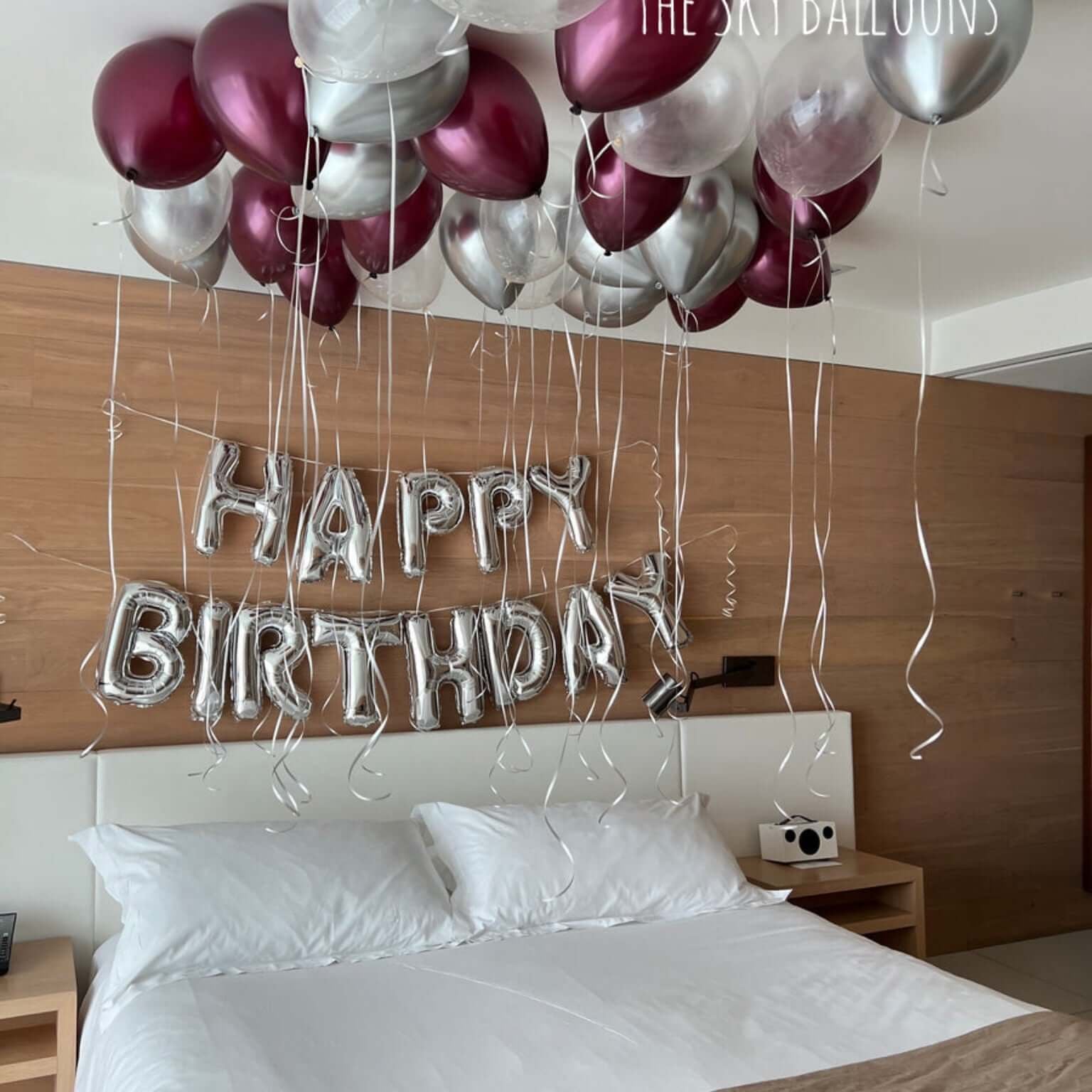Decorative balloons spelling 'Happy Birthday' above a bed in a bedroom.