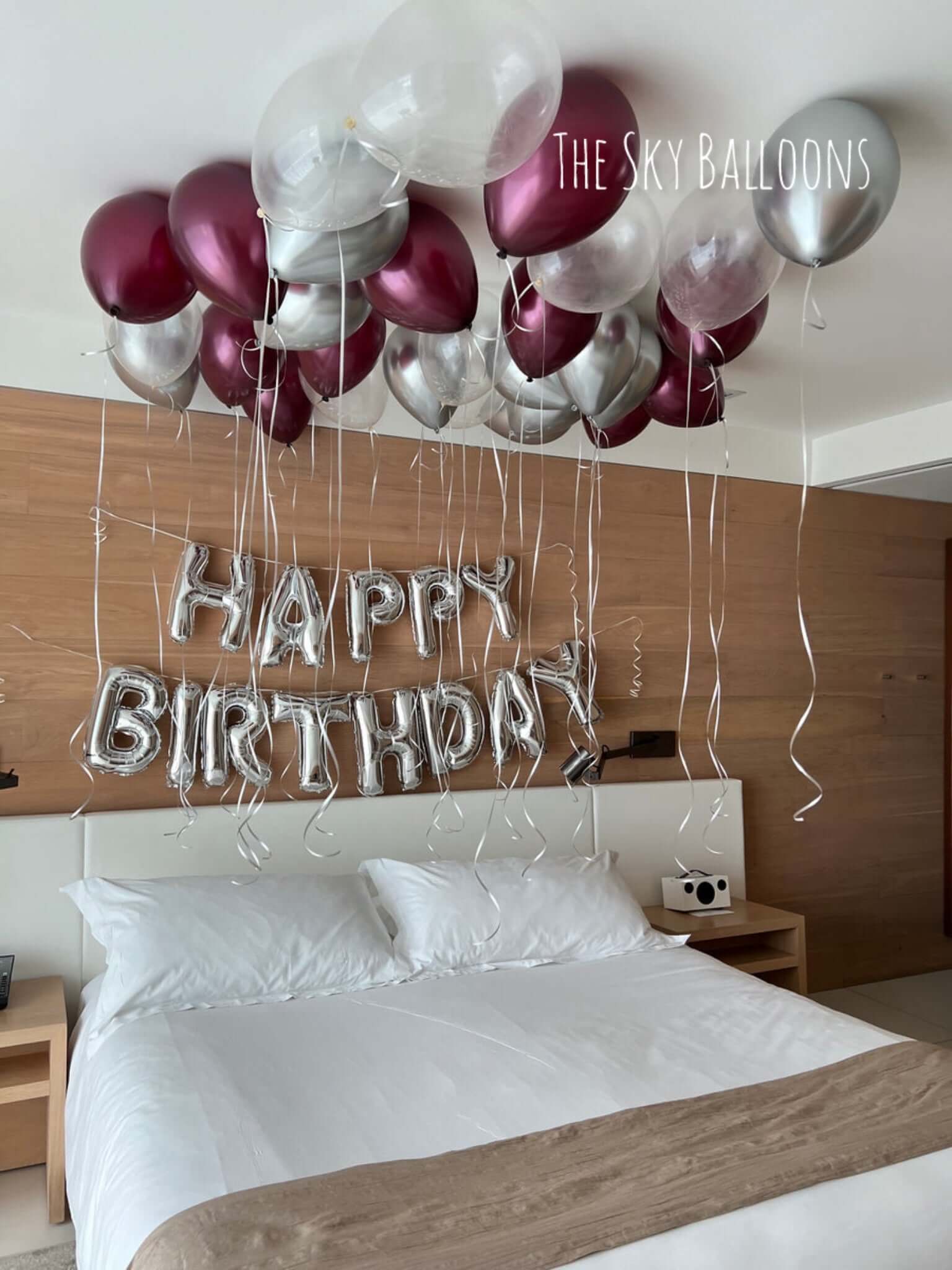 Decorative balloons spelling 'Happy Birthday' above a bed in a bedroom.
