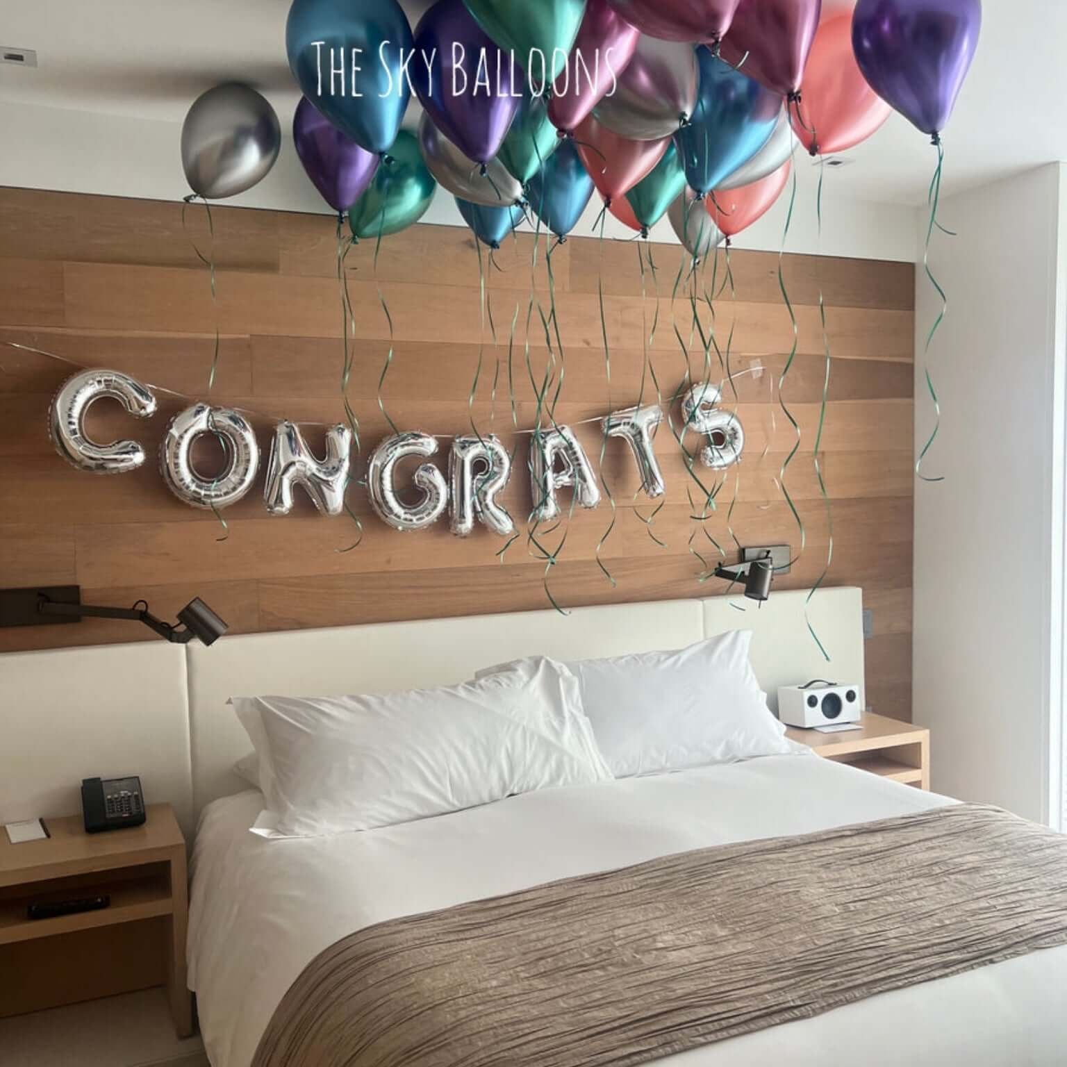 Decorative setup with balloons and 'CONGRATS' letters above a bed in a room.