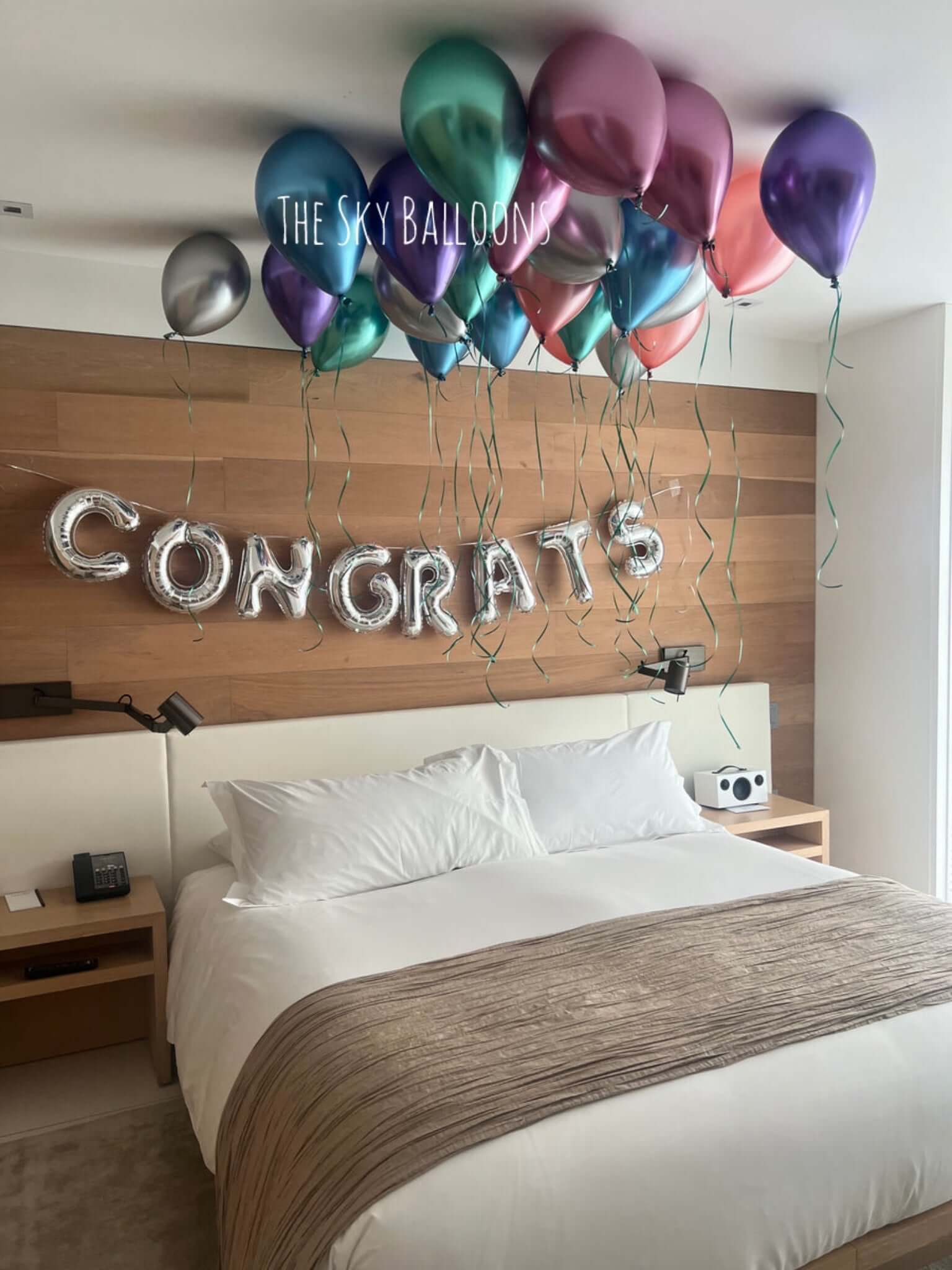 Decorative setup with balloons and 'CONGRATS' letters above a bed in a room.