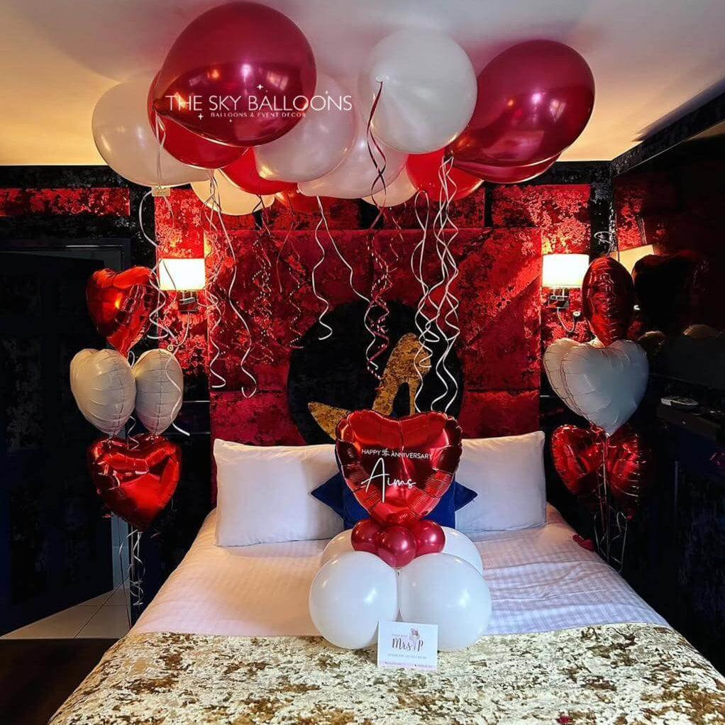 Decorative setup with balloons and heart shapes on a bed in a room.