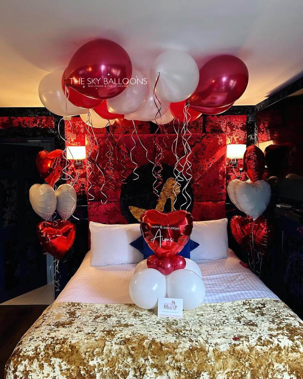 Decorative setup with balloons and heart shapes on a bed in a room.