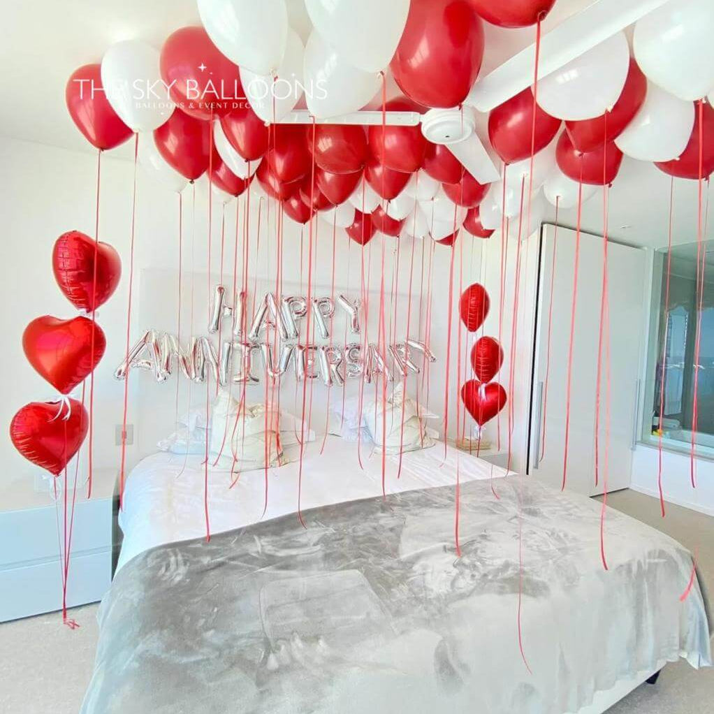 Decorative setup with red and white balloons and 'Happy Anniversary' text in a bedroom.