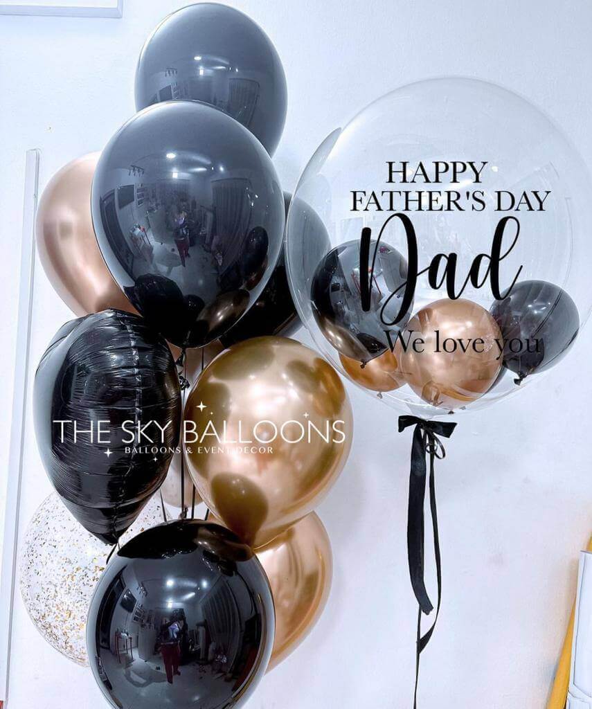 A bouquet of balloons including black and gold colors with 'Happy Father's Day' and 'We love you' text on a balloon, along with other balloons filled with helium gas.