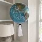 A balloon with a design resembling the Earth's globe and the text 'Dad you're our world' printed on it, adorned with tassels.