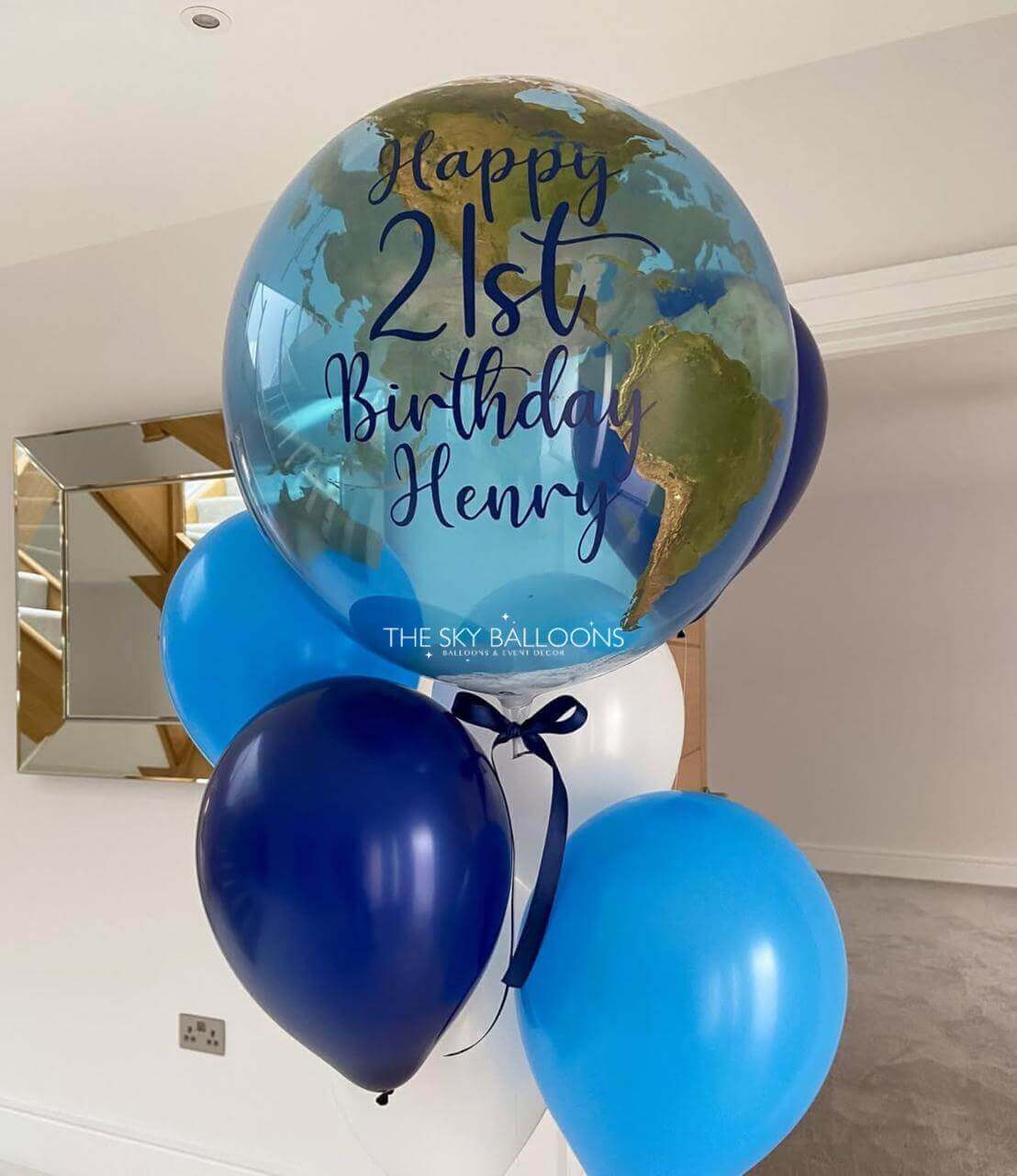 Globular balloon with 'Happy 21st Birthday Henry' text, surrounded by blue and navy balloons, against a neutral background.