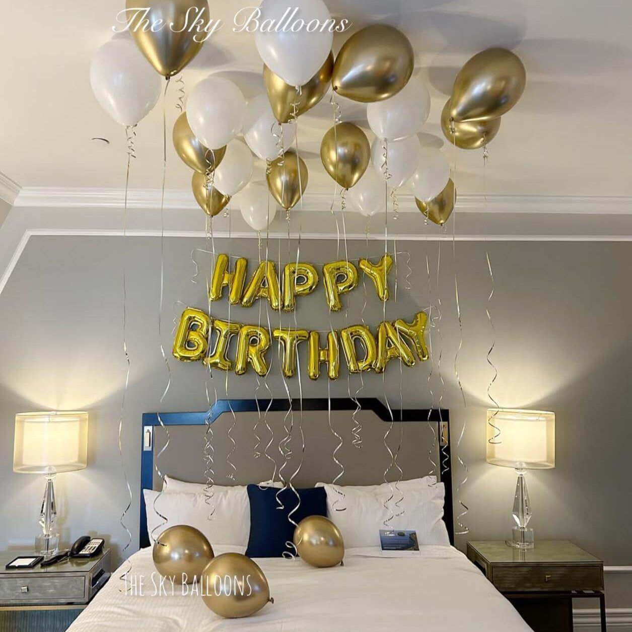 Gold Happy Birthday letter balloons with white and gold ceiling balloon display in elegant bedroom setting