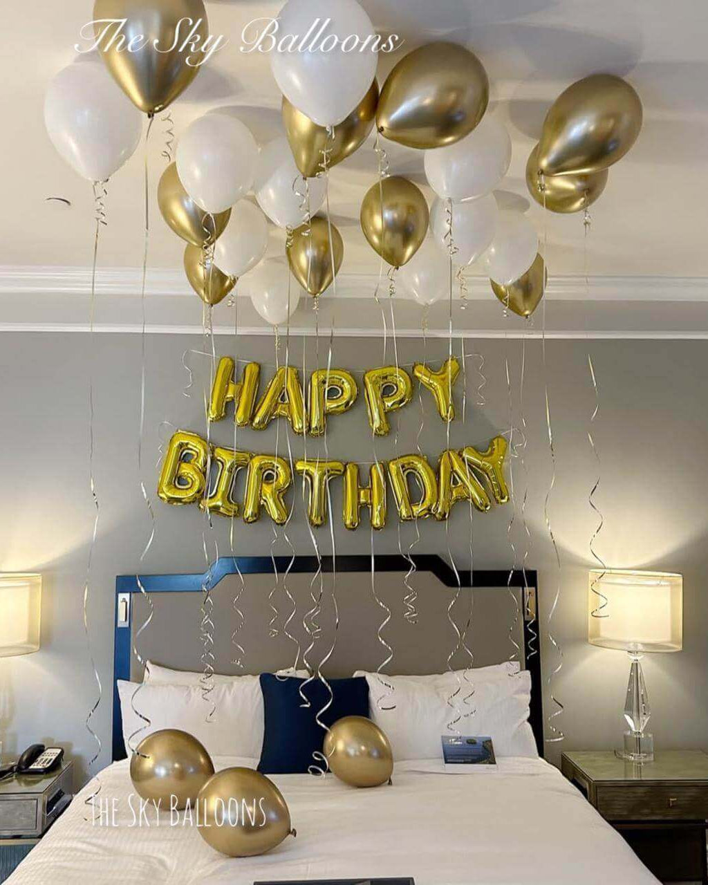 Gold Happy Birthday letter balloons with white and gold ceiling balloon display in elegant bedroom setting