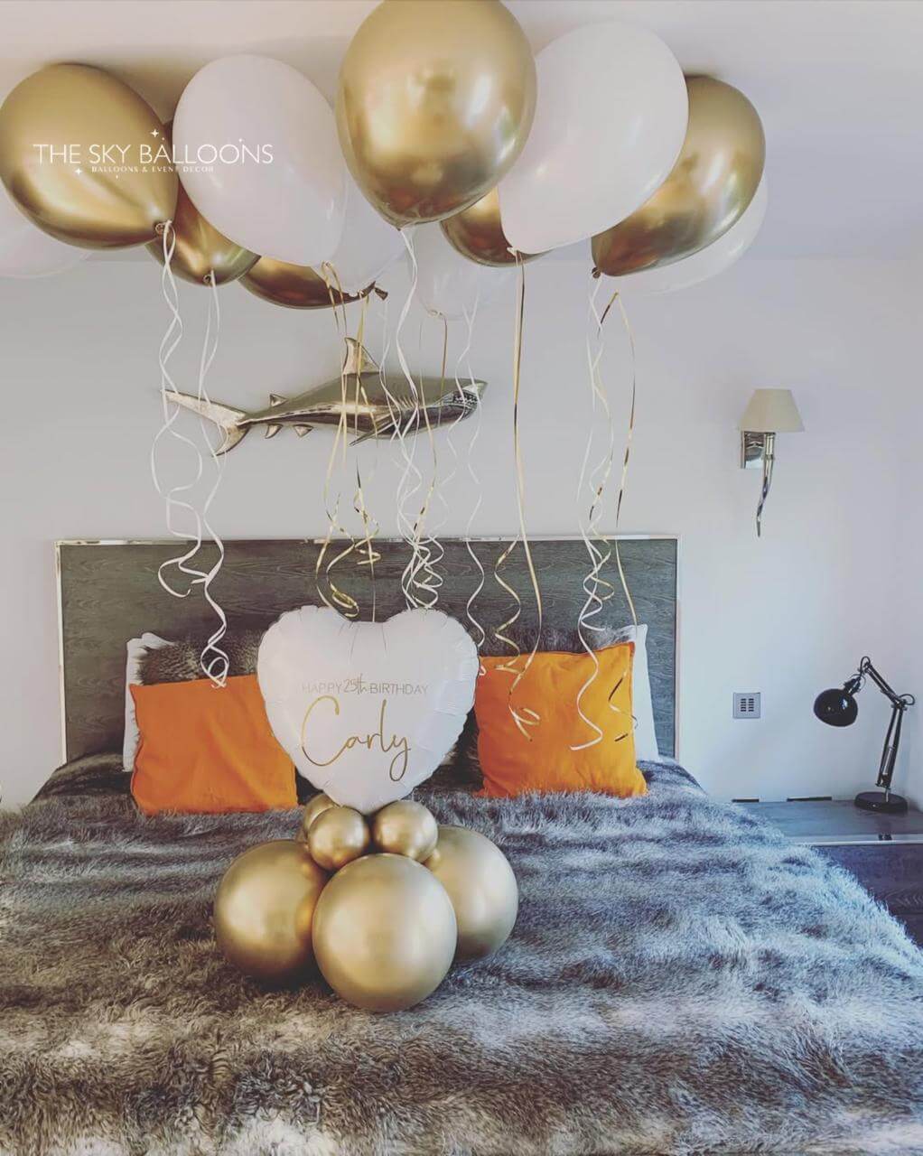 Decorative setup with gold and white balloons and a heart-shaped pillow on a bed.