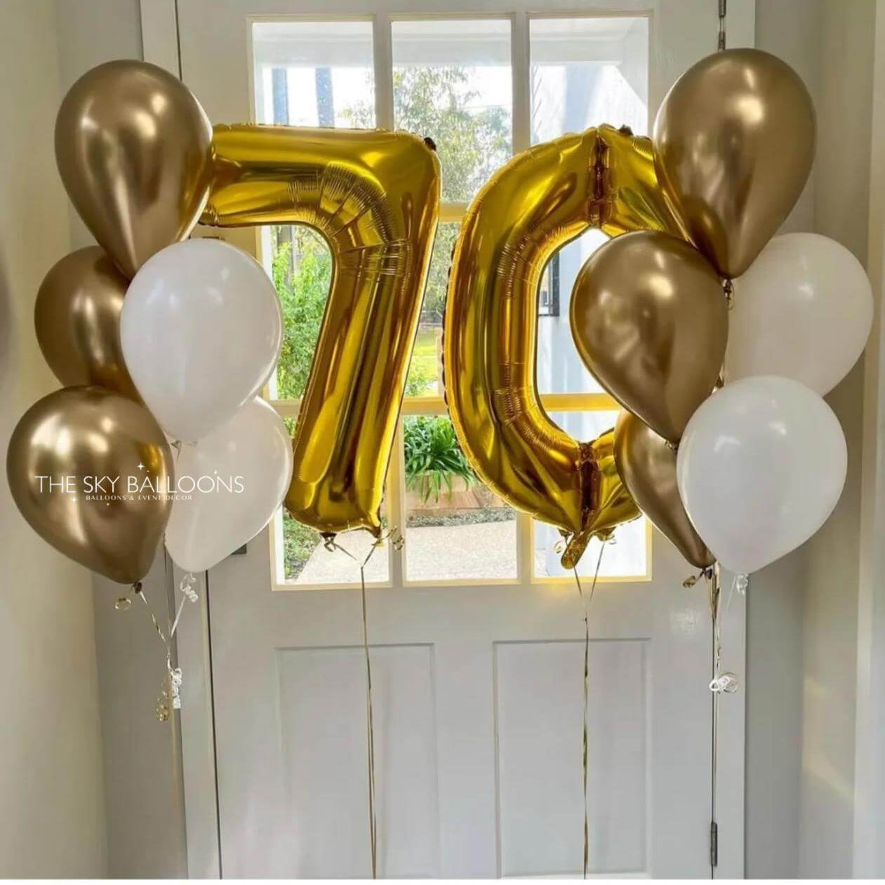Gold and white balloons with a number 70 balloon in front of a window.
