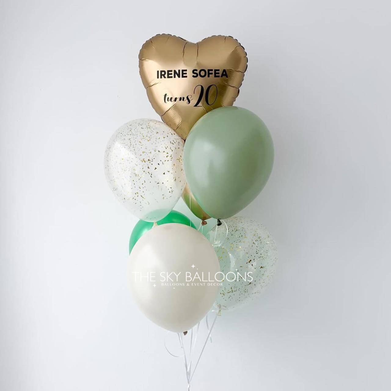 Gold heart-shaped balloon with 'IRENE SOFIA turns 20' text, surrounded by other balloons on a white background.