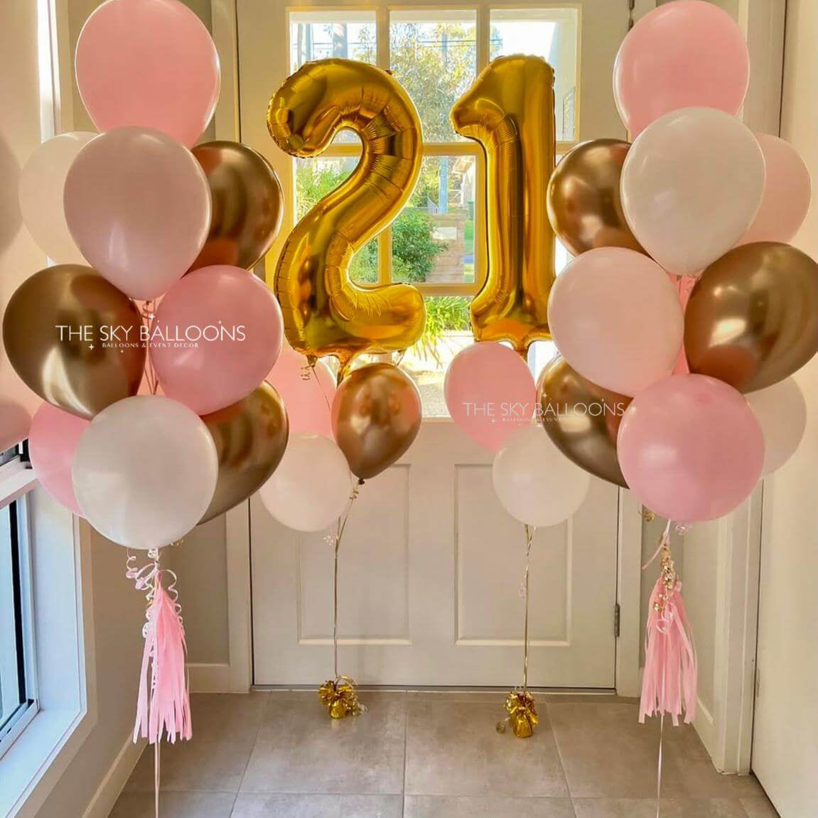 Gold number '21' balloon with pink, white, and gold balloons in a room.