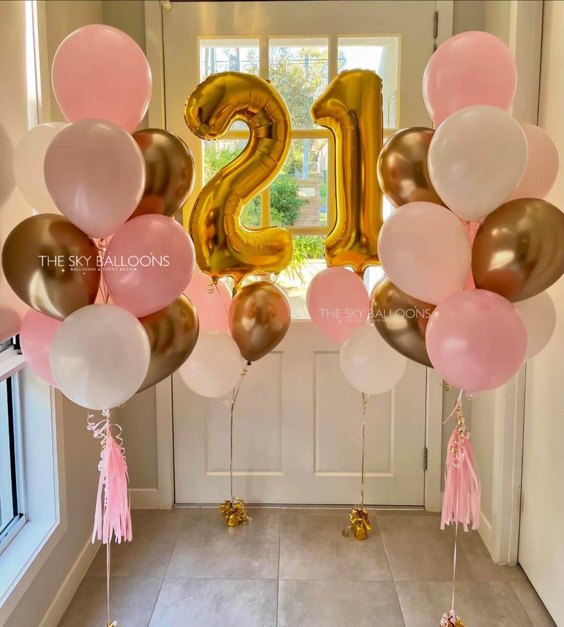 Gold number '21' balloon with pink, white, and gold balloons in a room.