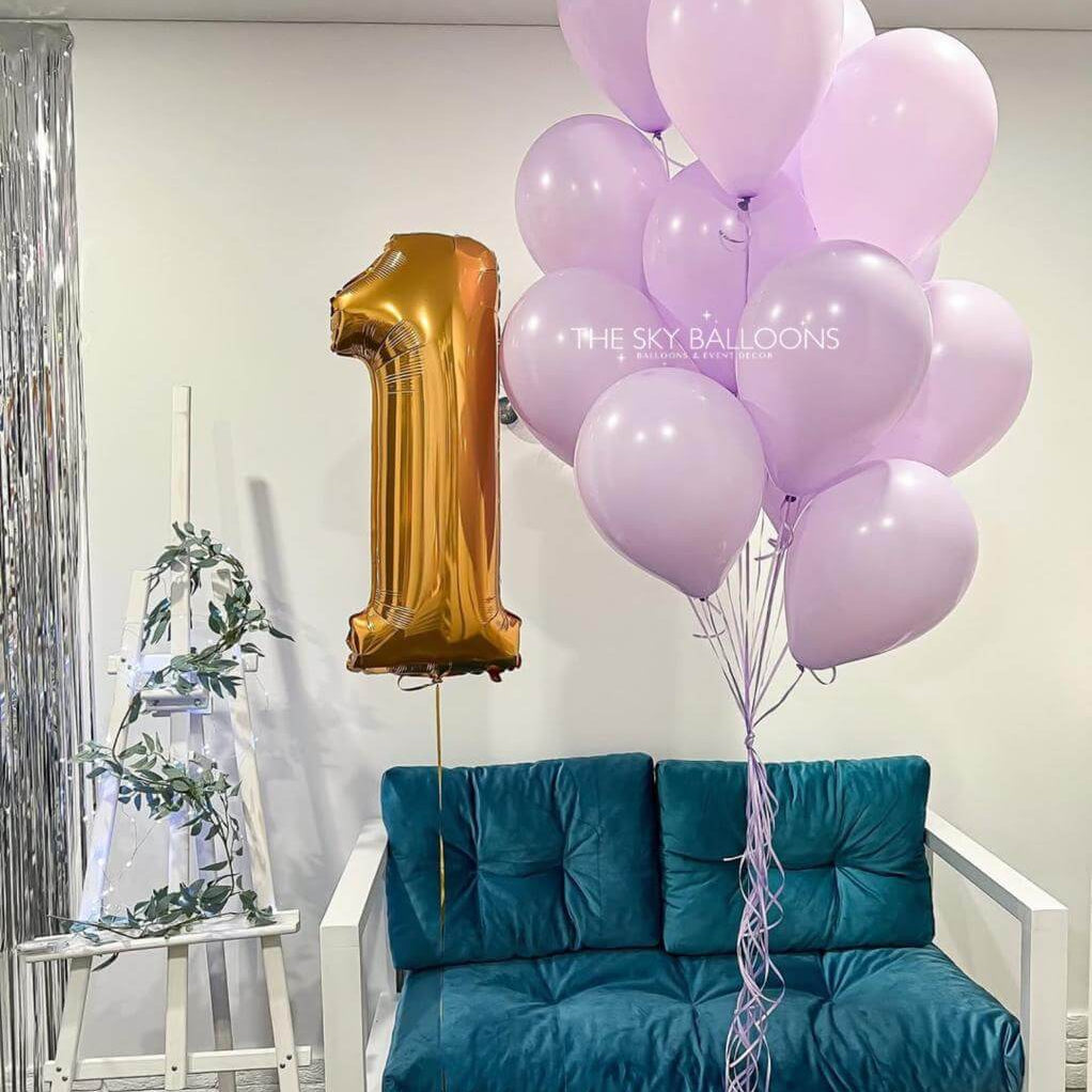 Gold number one balloon with pink balloons on a teal couch against a white wall.