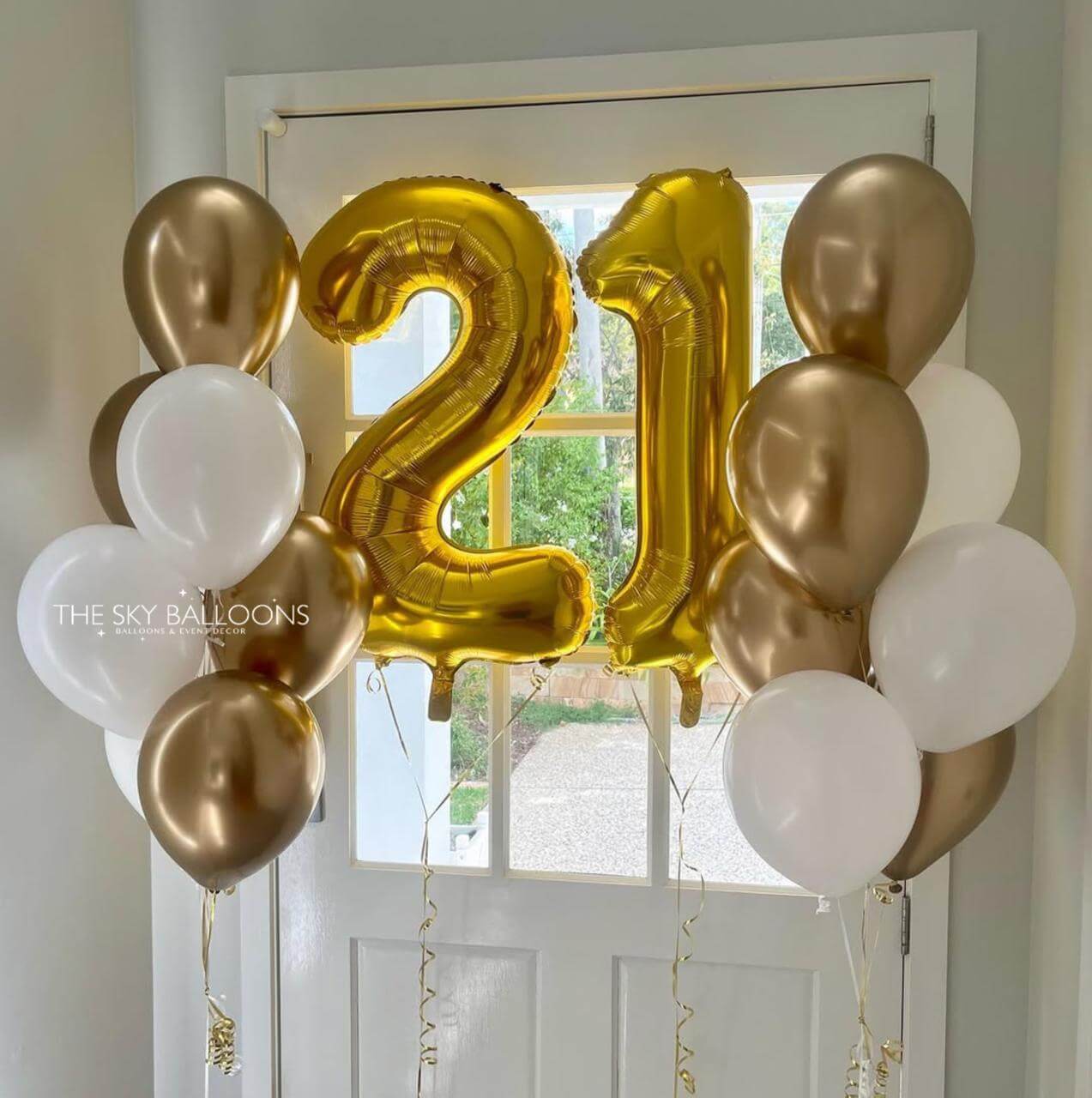 Gold, white, and bronze balloons with '21' shaped balloon on a door.