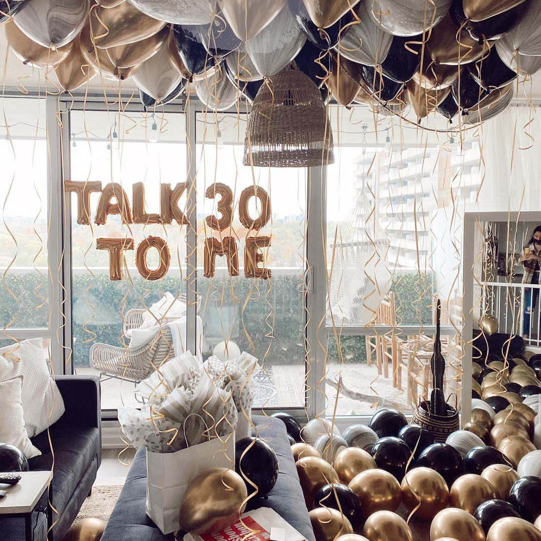 A room decorated with silver helium-filled balloons spelling out 'TALK TO ME' and other balloons on the floor.