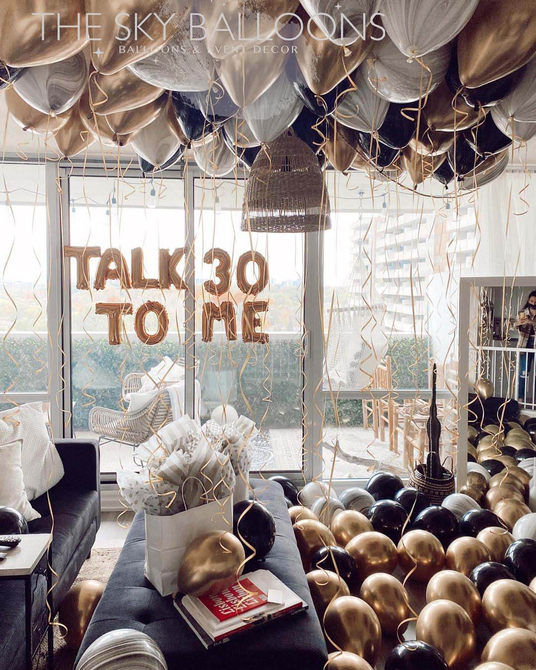 A room decorated with silver helium-filled balloons spelling out 'TALK TO ME' and other balloons on the floor.